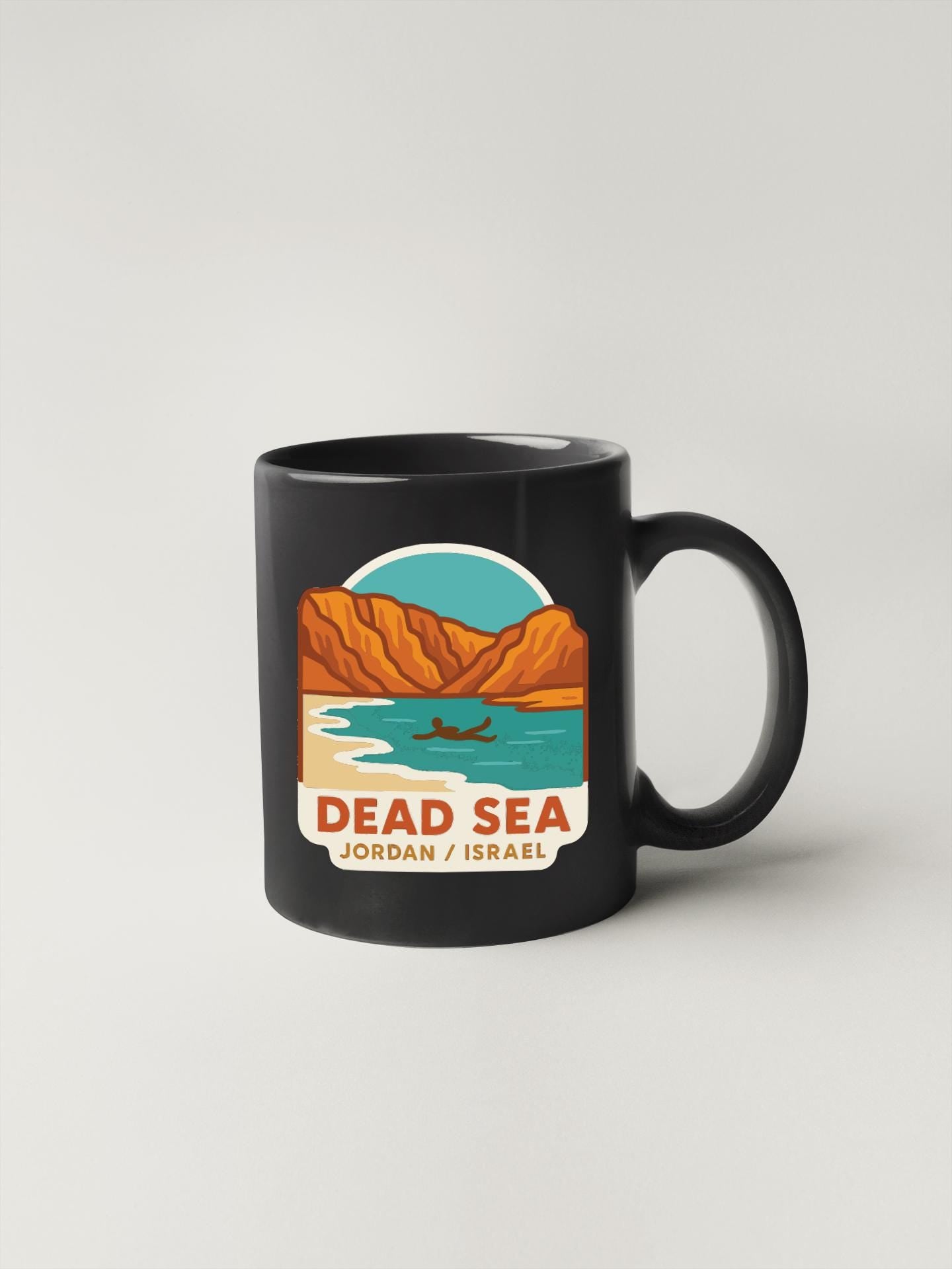A black coffee mug with a graphic design depicting a scenic landscape with mountains, a lake, and a boat.