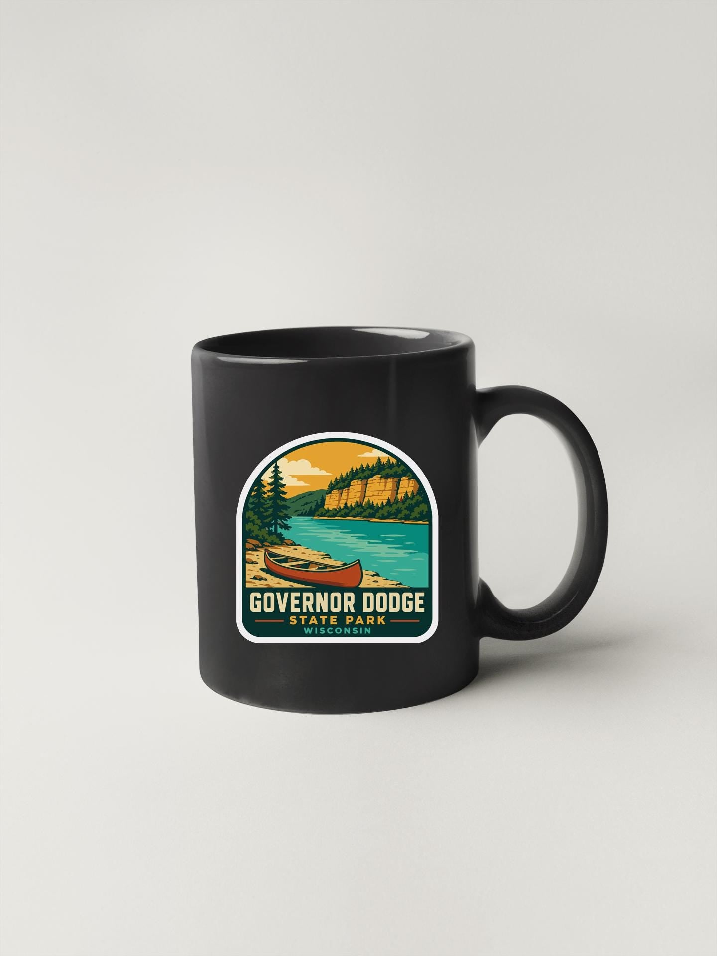 A black coffee mug with a sticker depicting a scenic landscape featuring a lake, mountains, and a canoe.