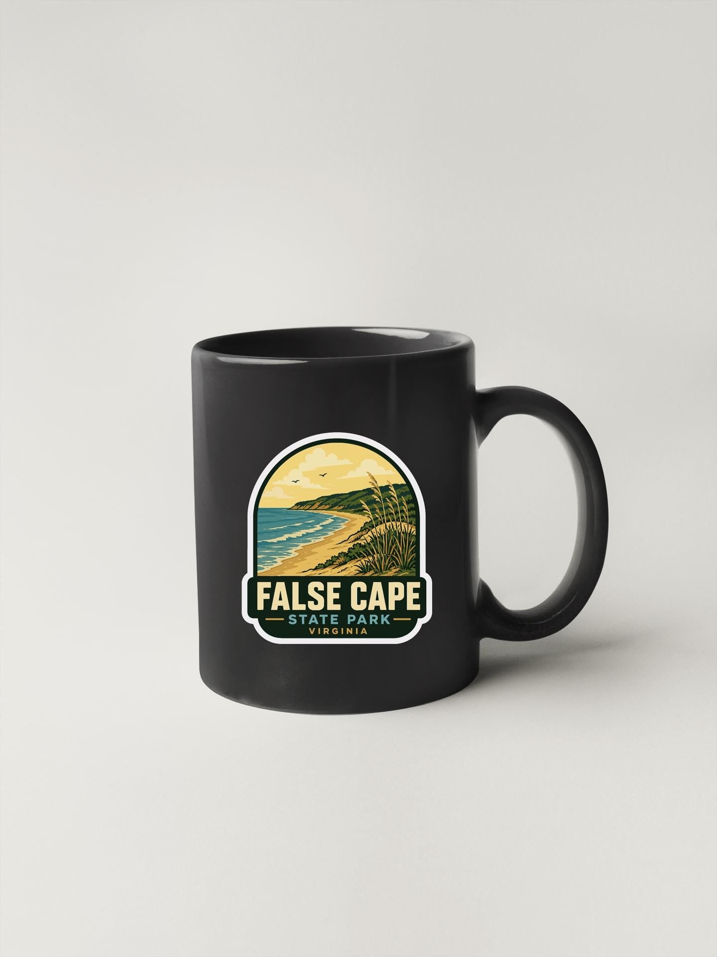 A black coffee mug with a graphic design depicting a coastal landscape, featuring the text "FALSE CAPE STATE PARK VIRGINIA".