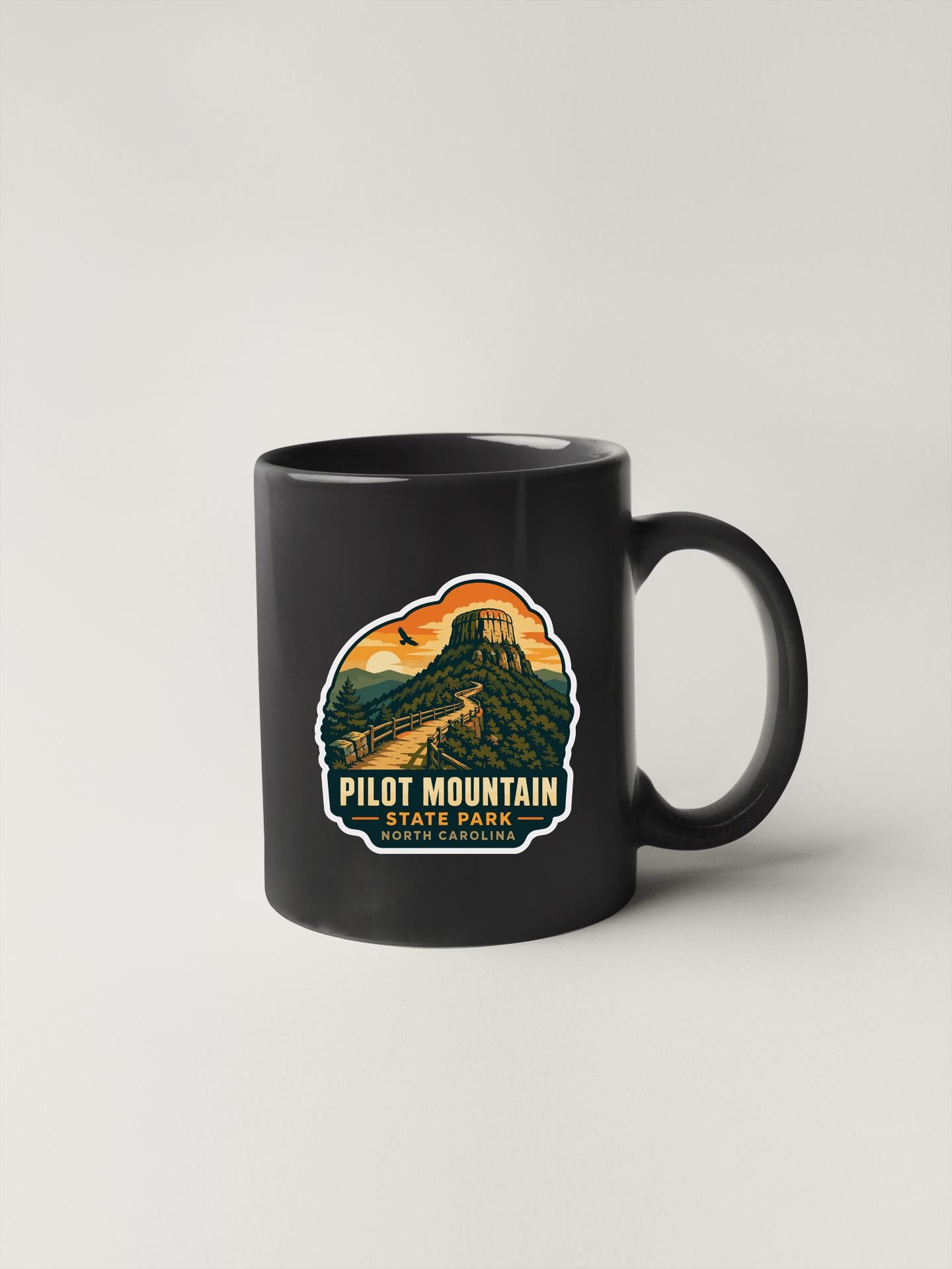 A black coffee mug with a graphic design depicting a mountain landscape and the text "PILOT MOUNTAIN STATE PARK NORTH DAKOTA, WYOMING" printed on it.