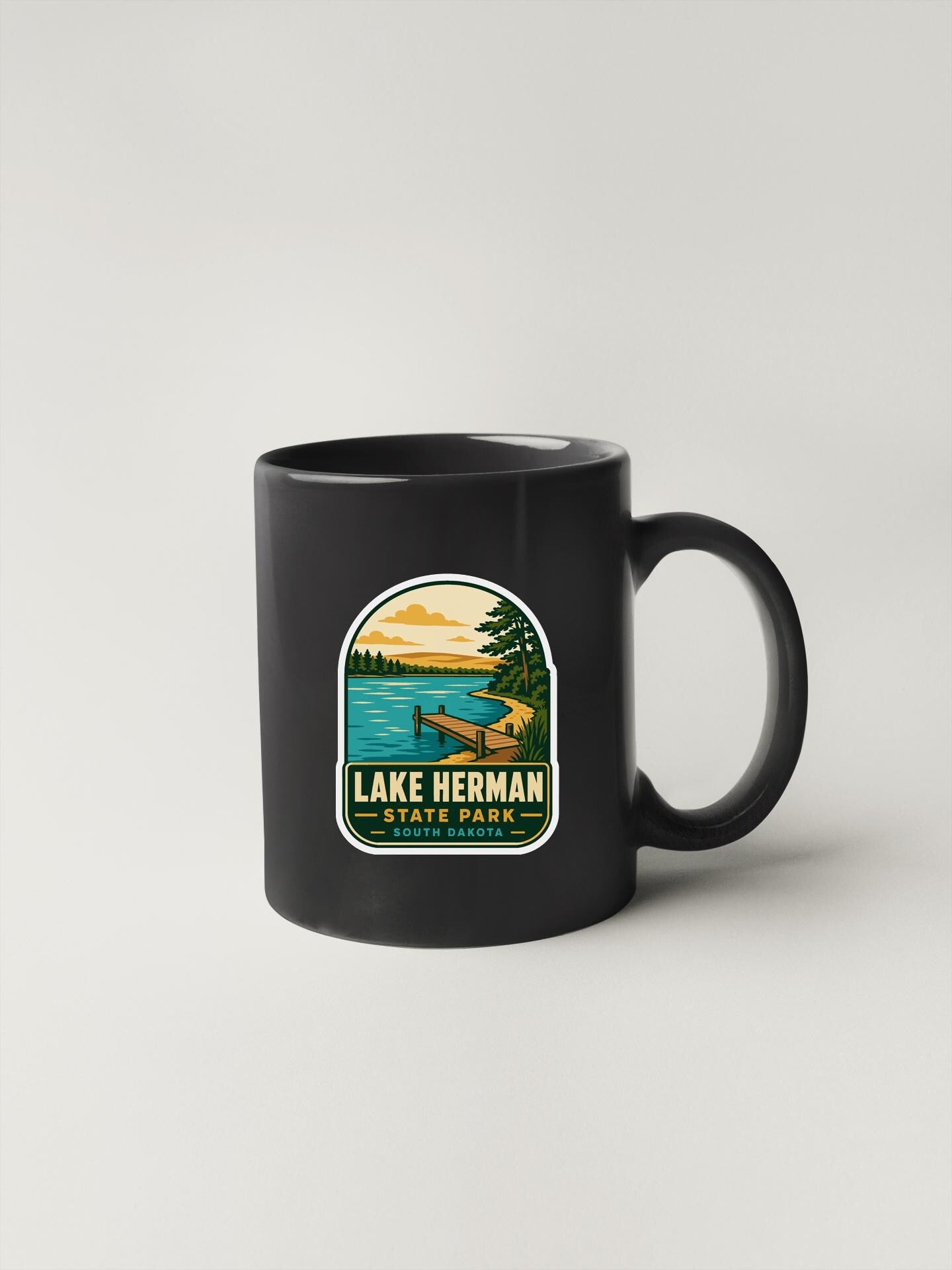 A black coffee mug with a sticker depicting Lake Herman State Park.