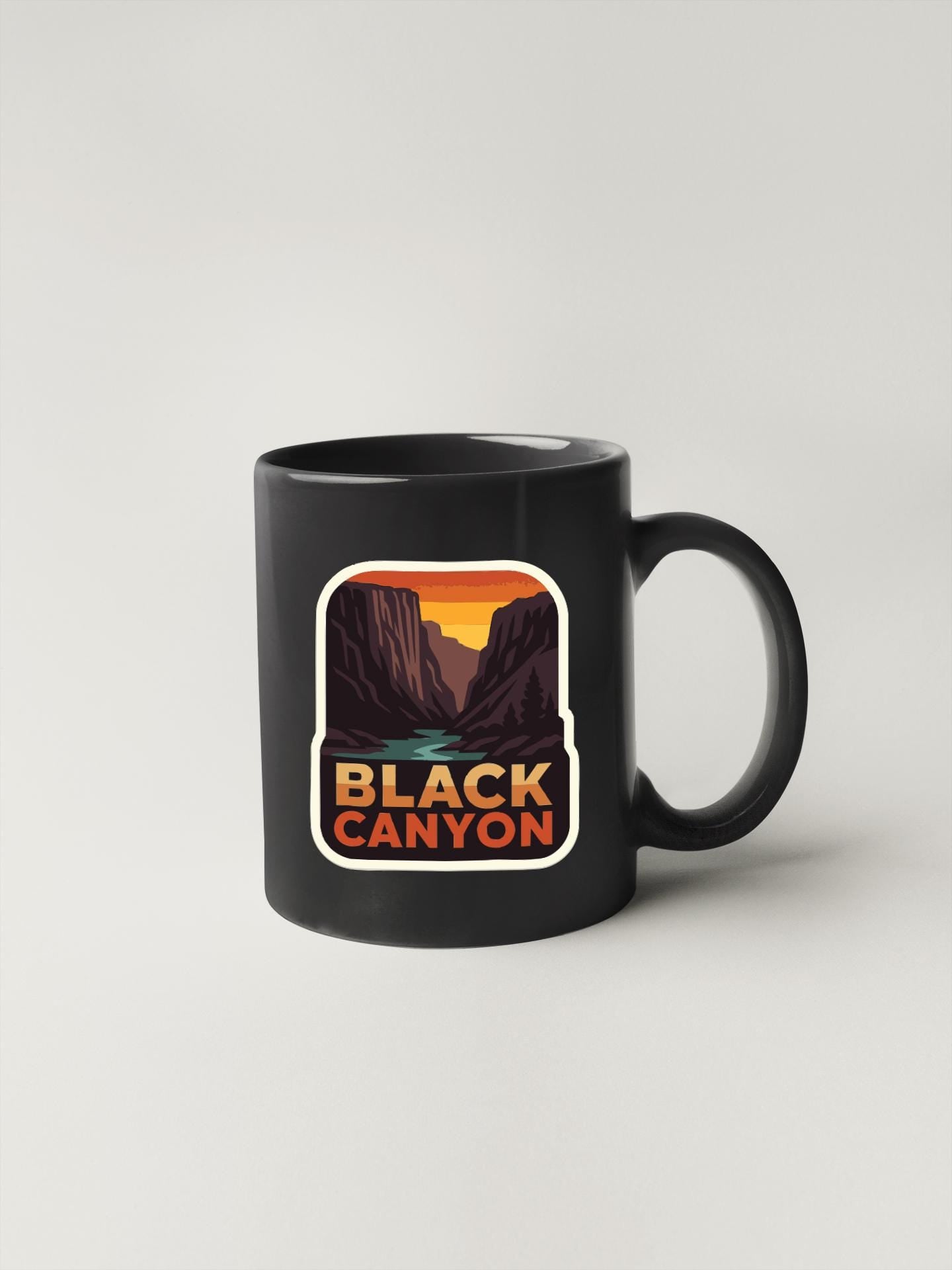 A black coffee mug with a graphic design depicting a scenic mountain landscape, specifically Black Canyon.
