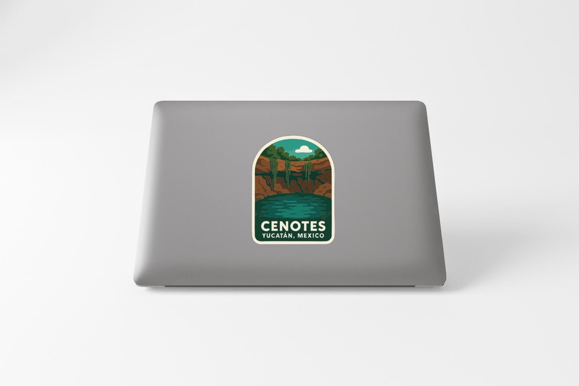 a sticker on a laptop that displays the text "CENOTES YUCATÁN, MEXICO" along with an illustration of a mountain landscape.