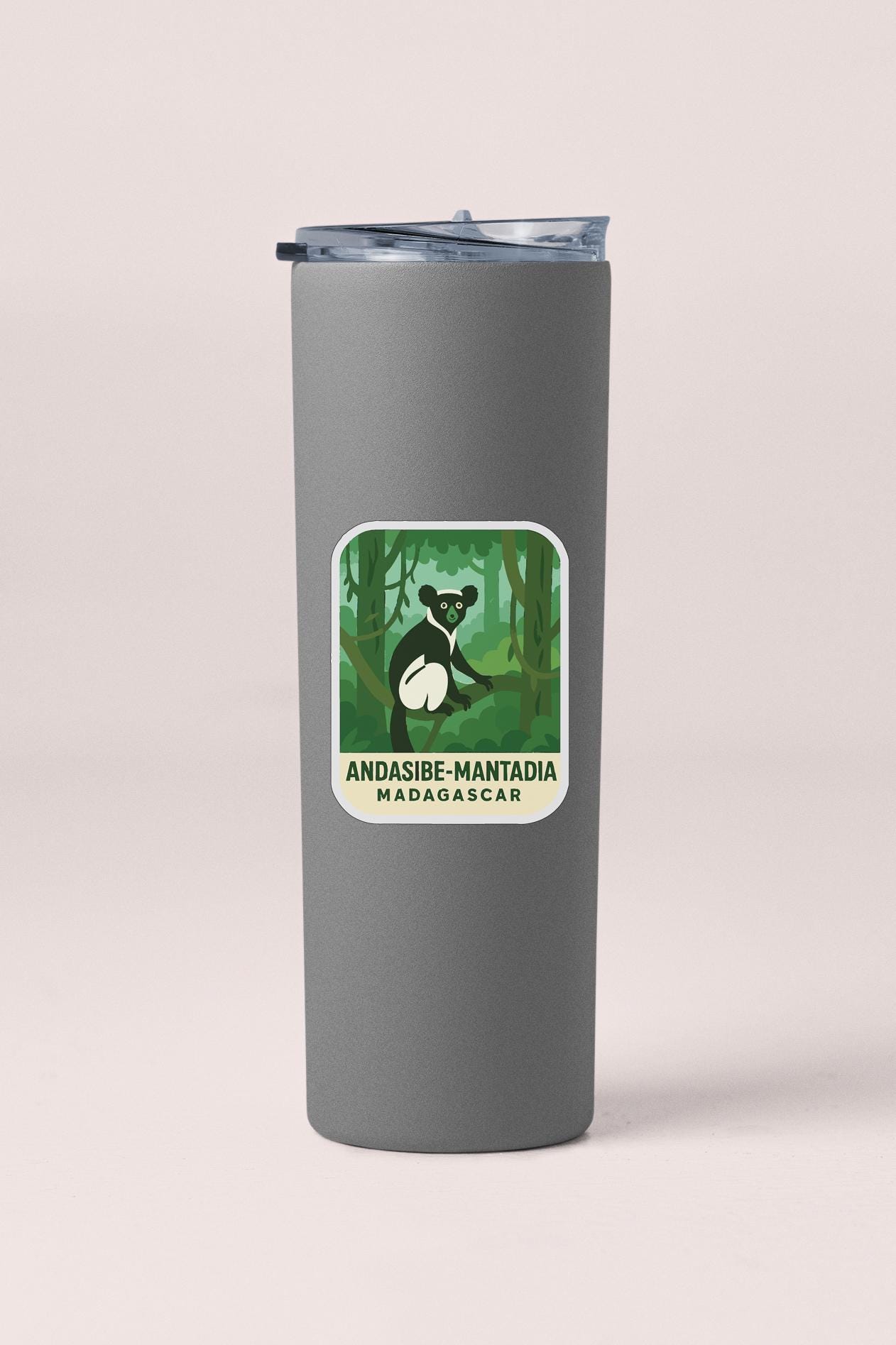 A gray tumbler with a sticker depicting a black and white bear in a jungle setting.