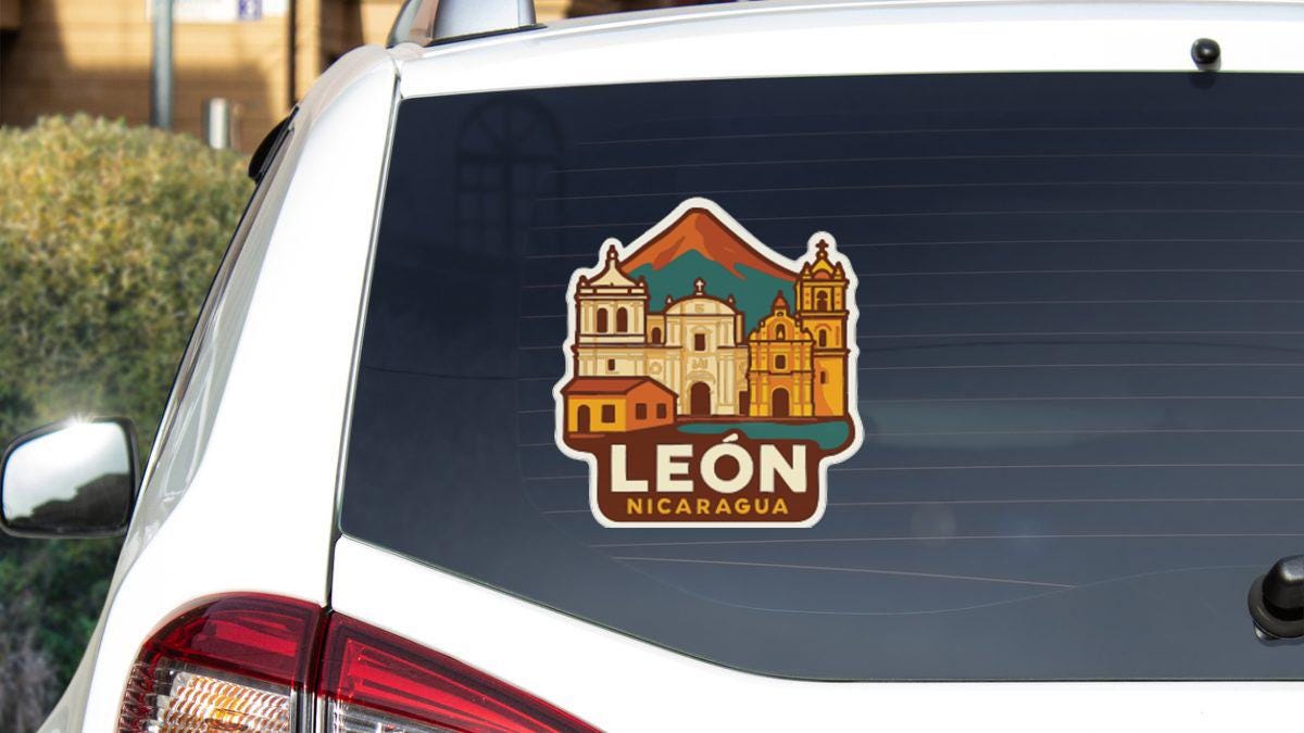 A sticker on the rear window of a white car, depicting a cityscape with buildings and a mountain.