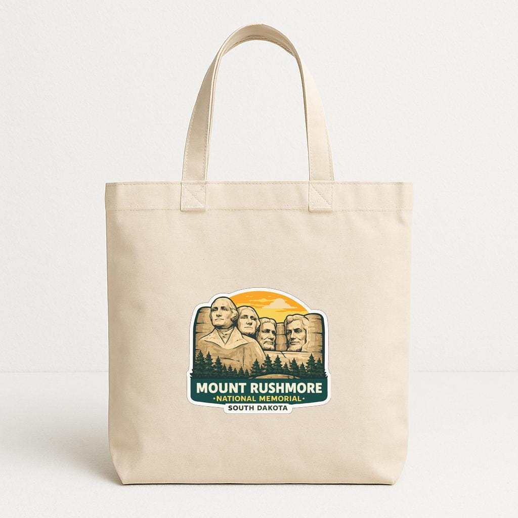 A beige tote bag with a printed design featuring the Statue of Liberty and Mount Rushmore, a famous landmark in South Dakota.