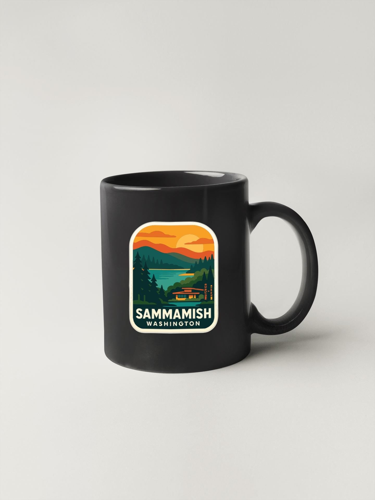 A black coffee mug with a graphic design depicting a scenic landscape with mountains, trees, and a lake.