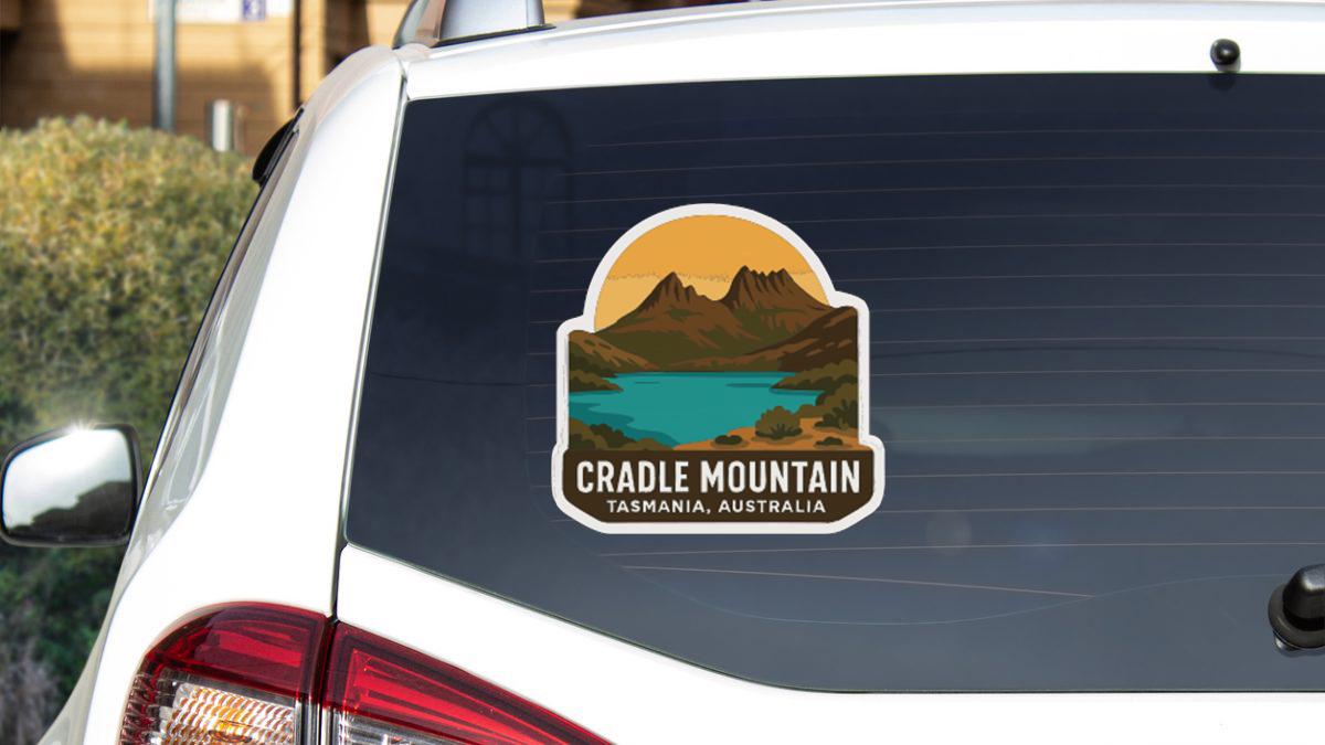 a sticker on the rear window of a white car, depicting a scenic landscape with mountains, a lake, and a sunset.