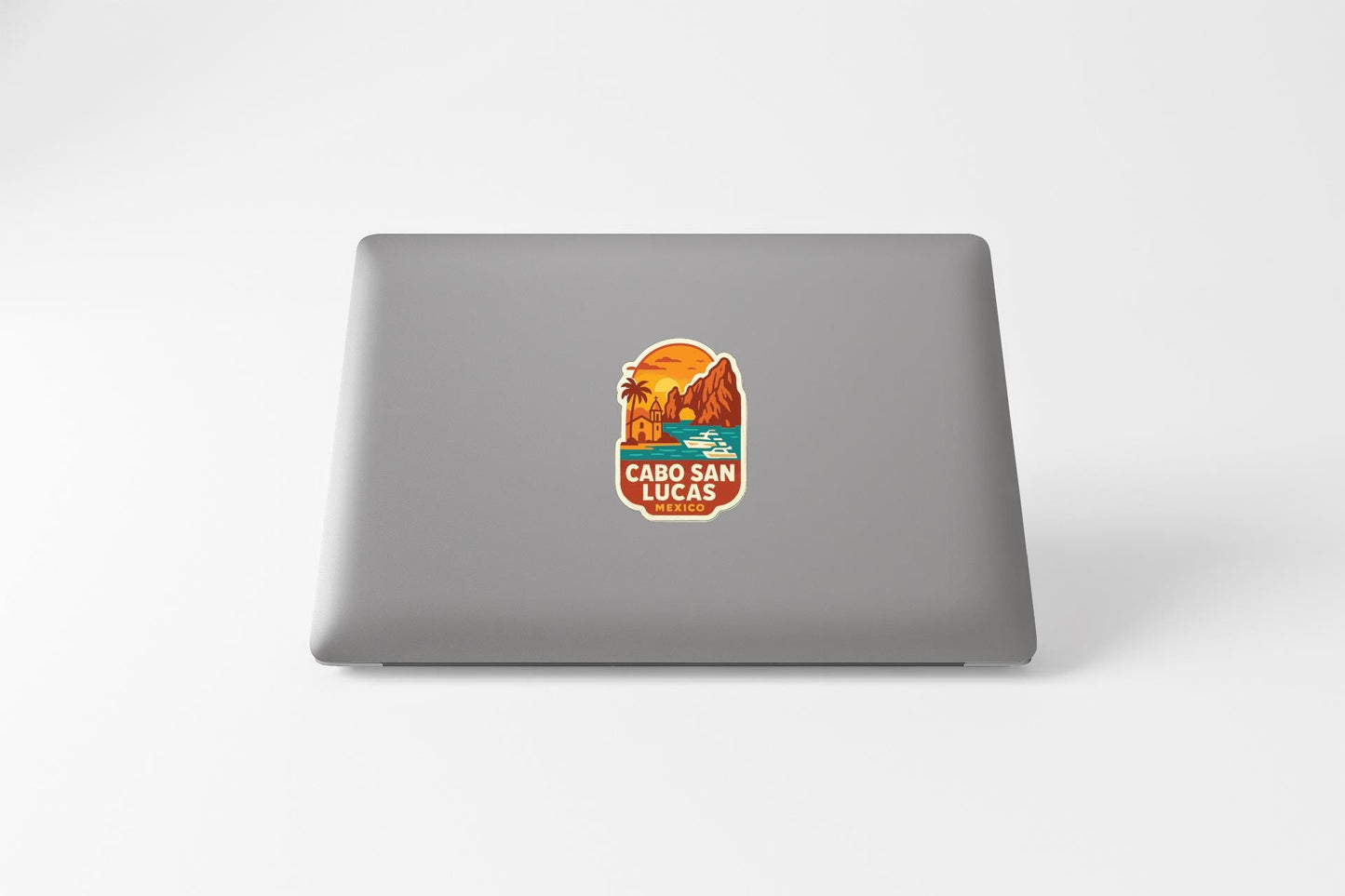A sticker on the back of a laptop, depicting a scenic landscape with mountains, palm trees, and a sunset.