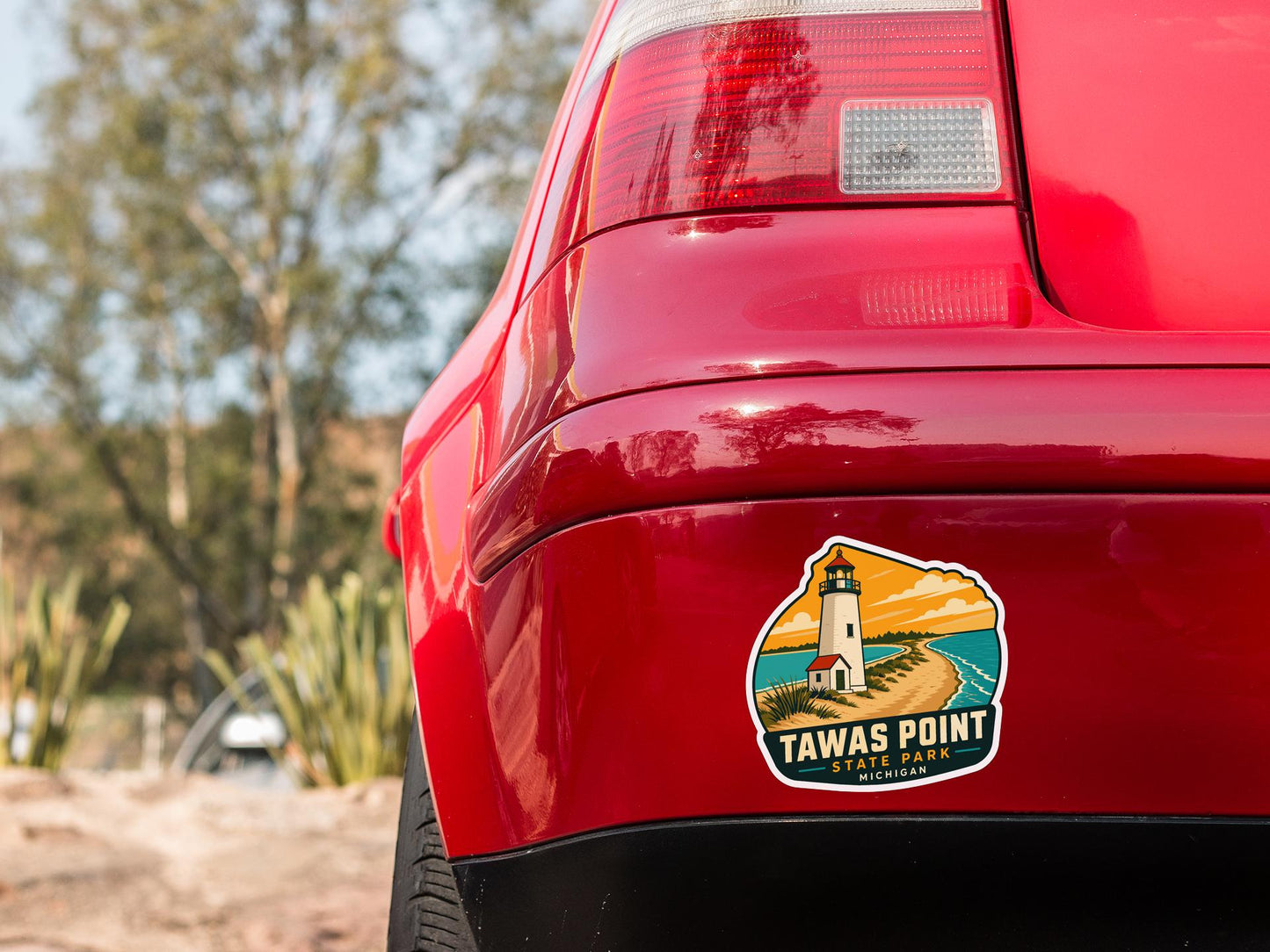 the rear end of a red car with a sticker on the trunk that says "Tawas Point State Park, Michigan".