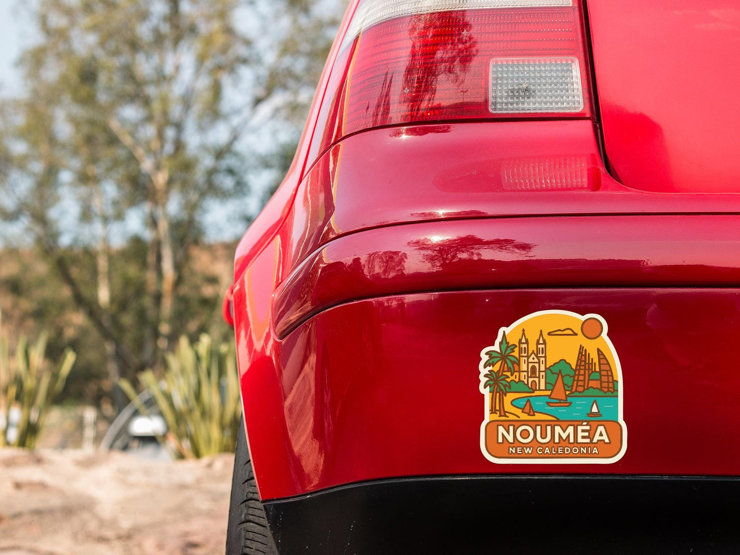 the rear end of a red car with a sticker on the trunk that features a tropical beach scene with palm trees and a castle.