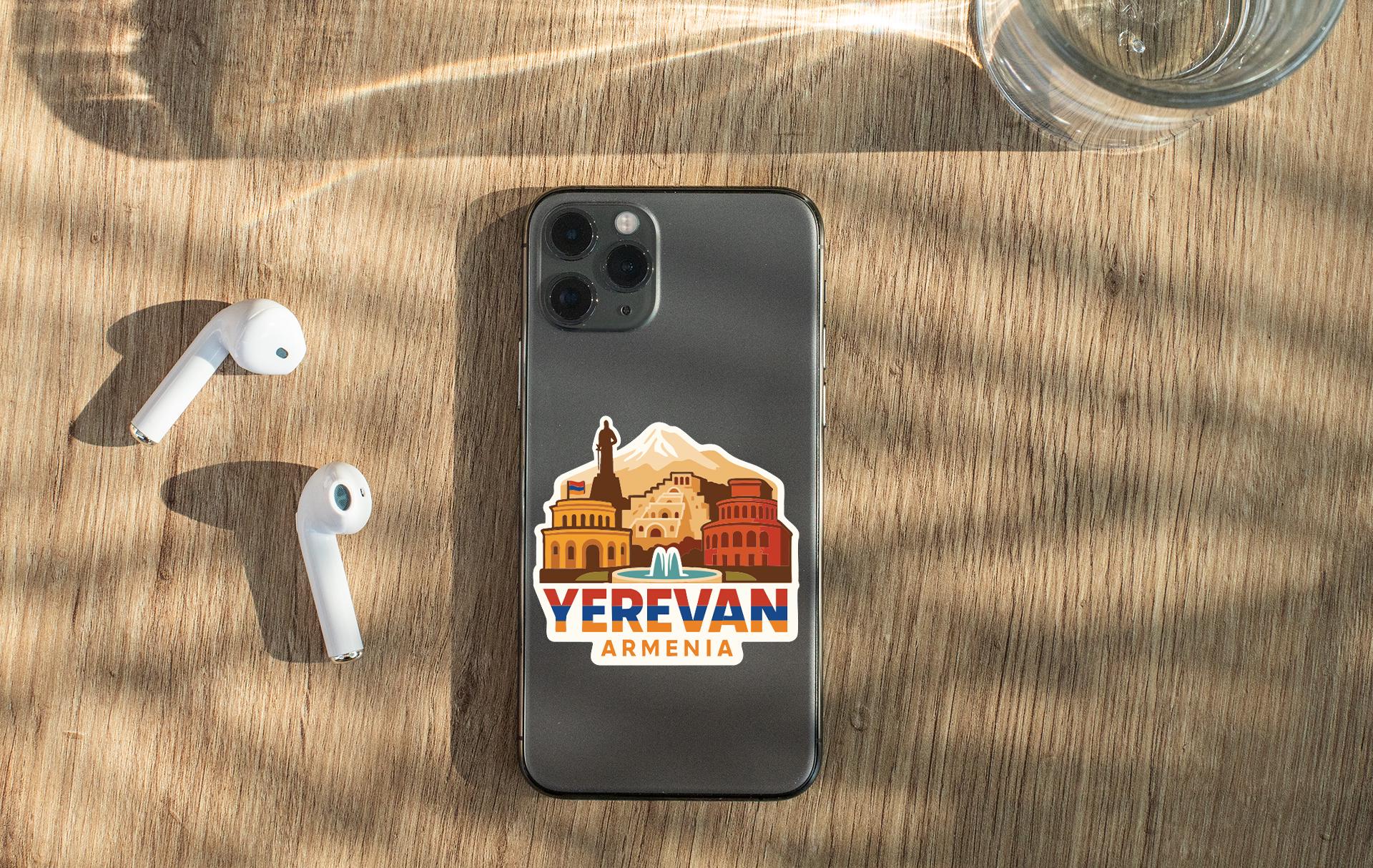 a smartphone with a sticker of Armenia on its back, placed on a wooden surface alongside a pair of white earbuds and a glass of water.