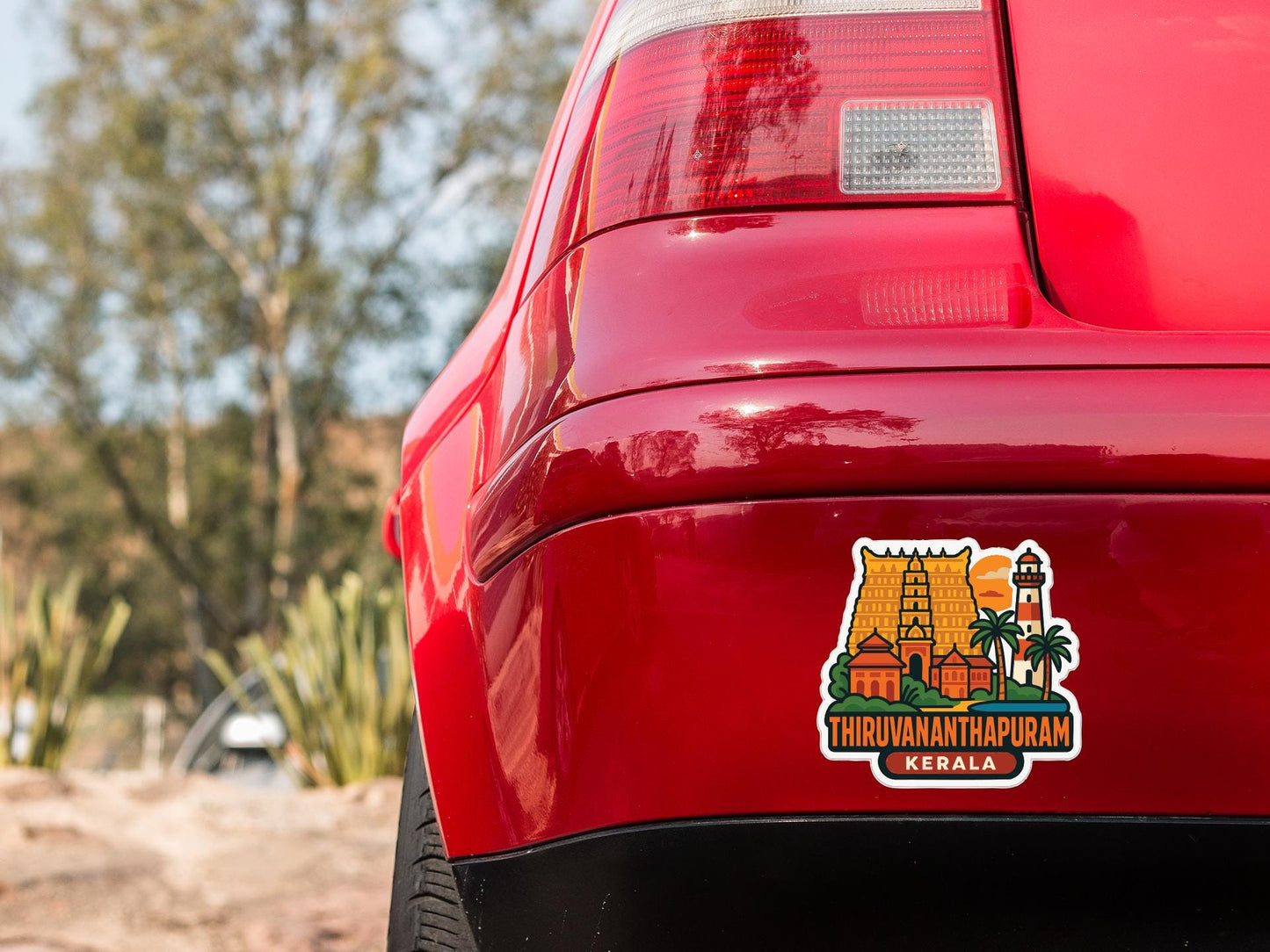 the rear end of a red car with a sticker on the trunk that features a tropical landscape and the text "Thiruvannanathanpuram, Kerala".