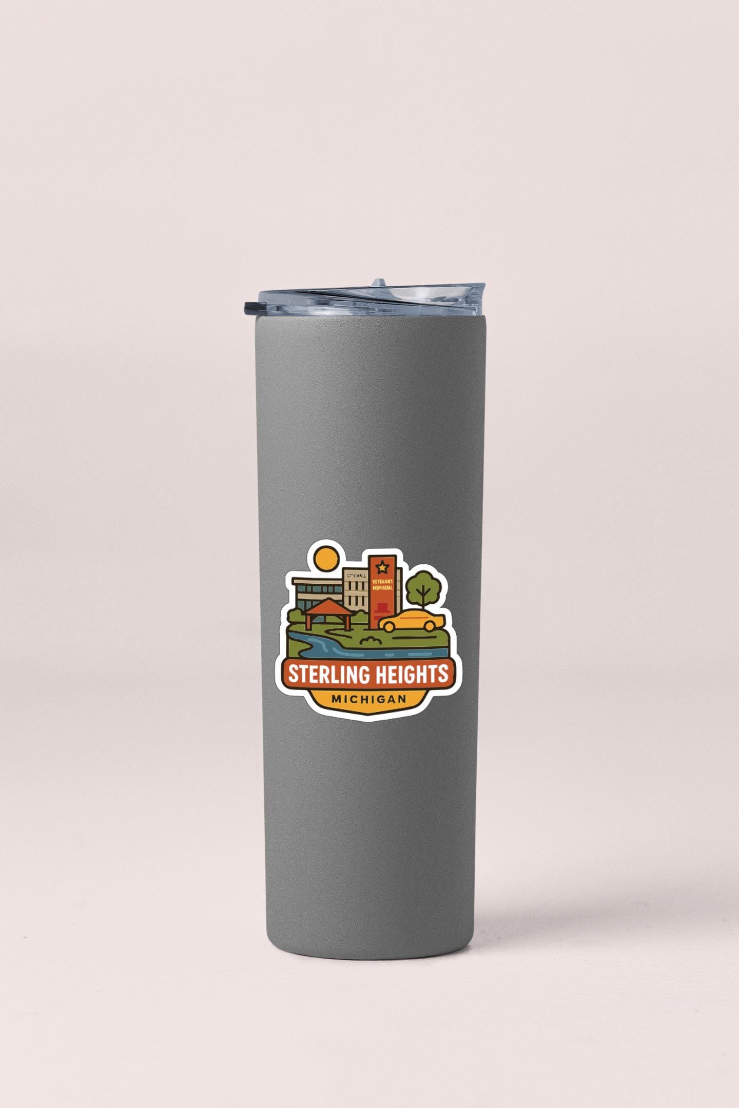 A gray insulated tumbler with a lid and a sticker depicting a cityscape with the text "Sterling Heights, Michigan".