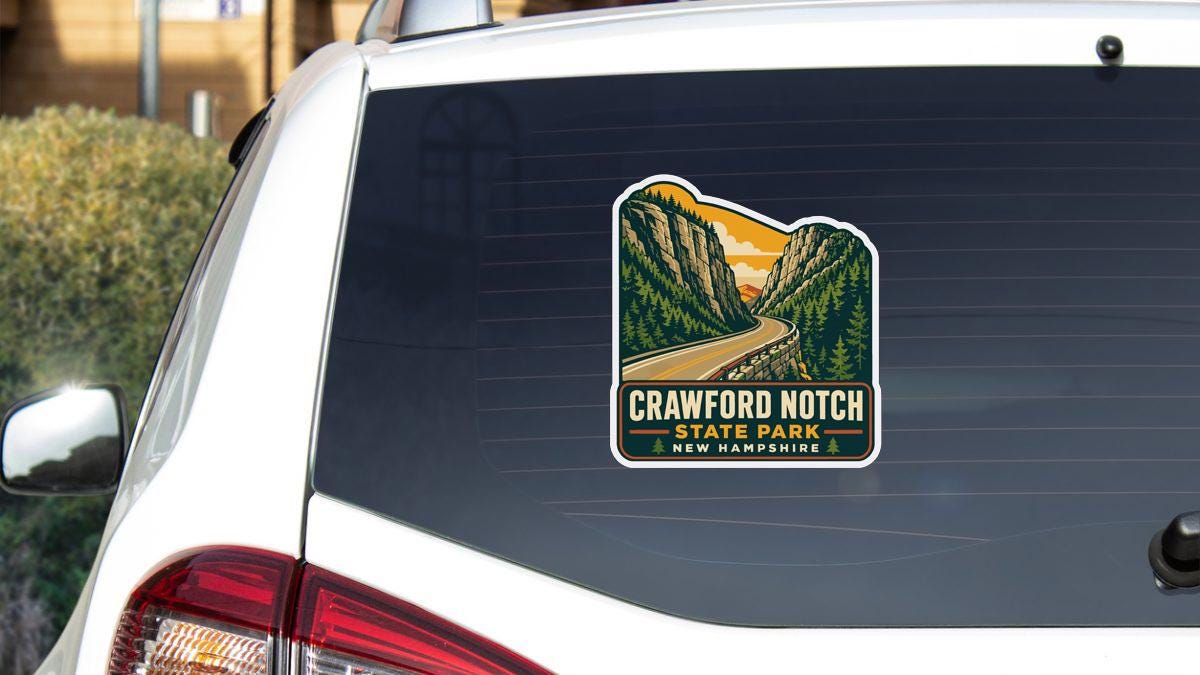 A sticker on the rear window of a white vehicle, depicting a scenic mountain landscape with a winding road.