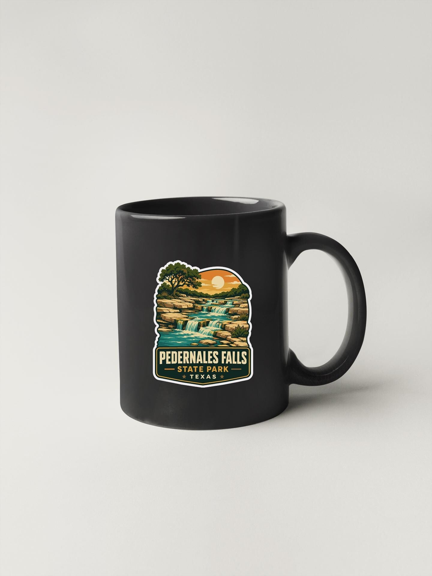 A black coffee mug with a graphic design depicting a waterfall and sunset.