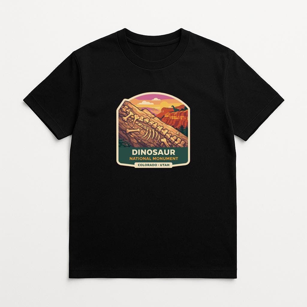 A black t-shirt with a graphic design depicting a dinosaur skeleton and the text "DINOSAUR" and "COLORADO - UTA".