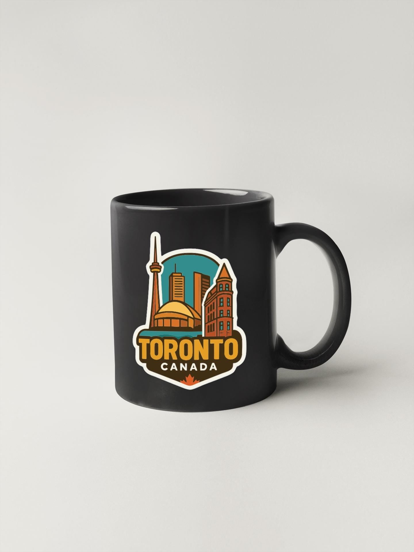 A black coffee mug with a colorful graphic of the Toronto skyline and the text "TORONTO CANADA" printed on it.