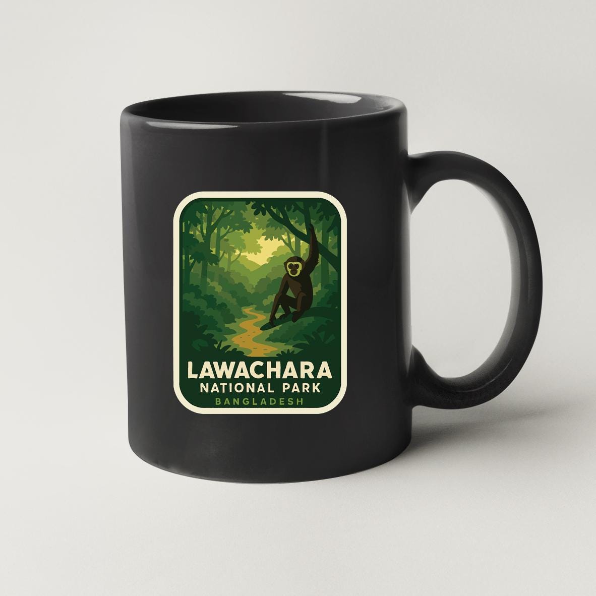A black coffee mug with a label that features an illustration of a monkey in a jungle setting, along with the text "LAWACHARA NATIONAL PARK BANGLADESH".