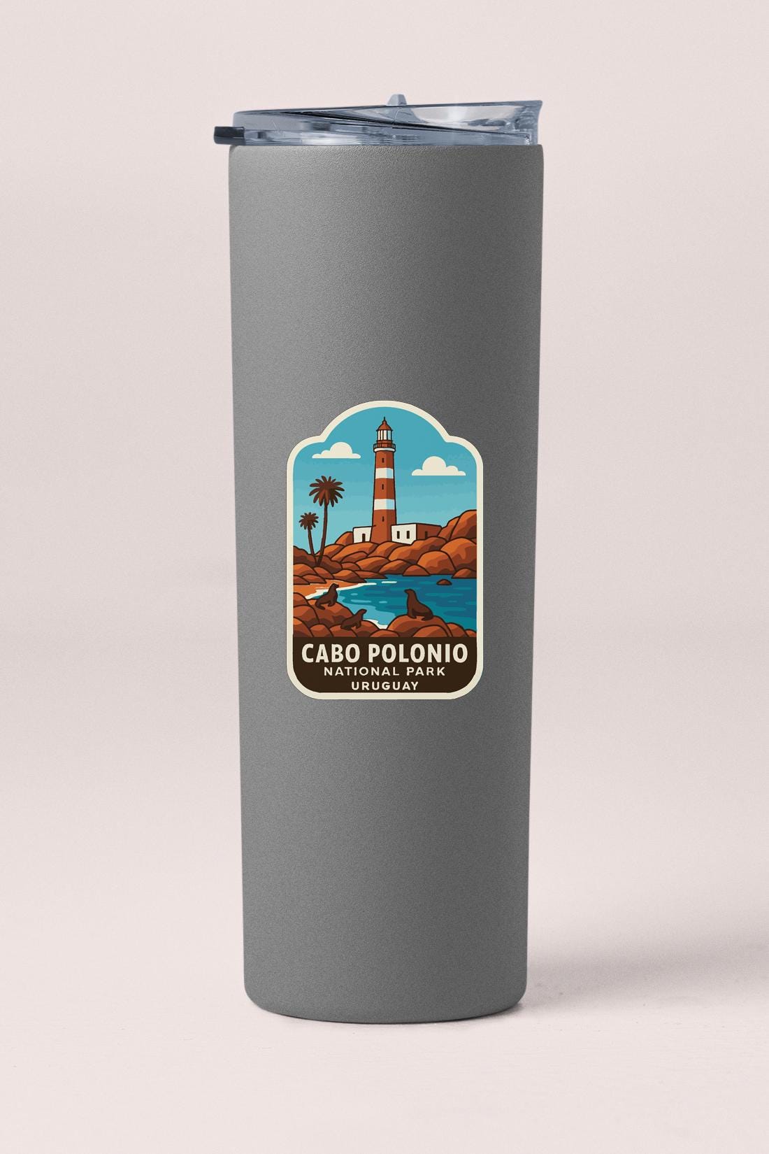 A gray tumbler with a label featuring a lighthouse and a beach scene.