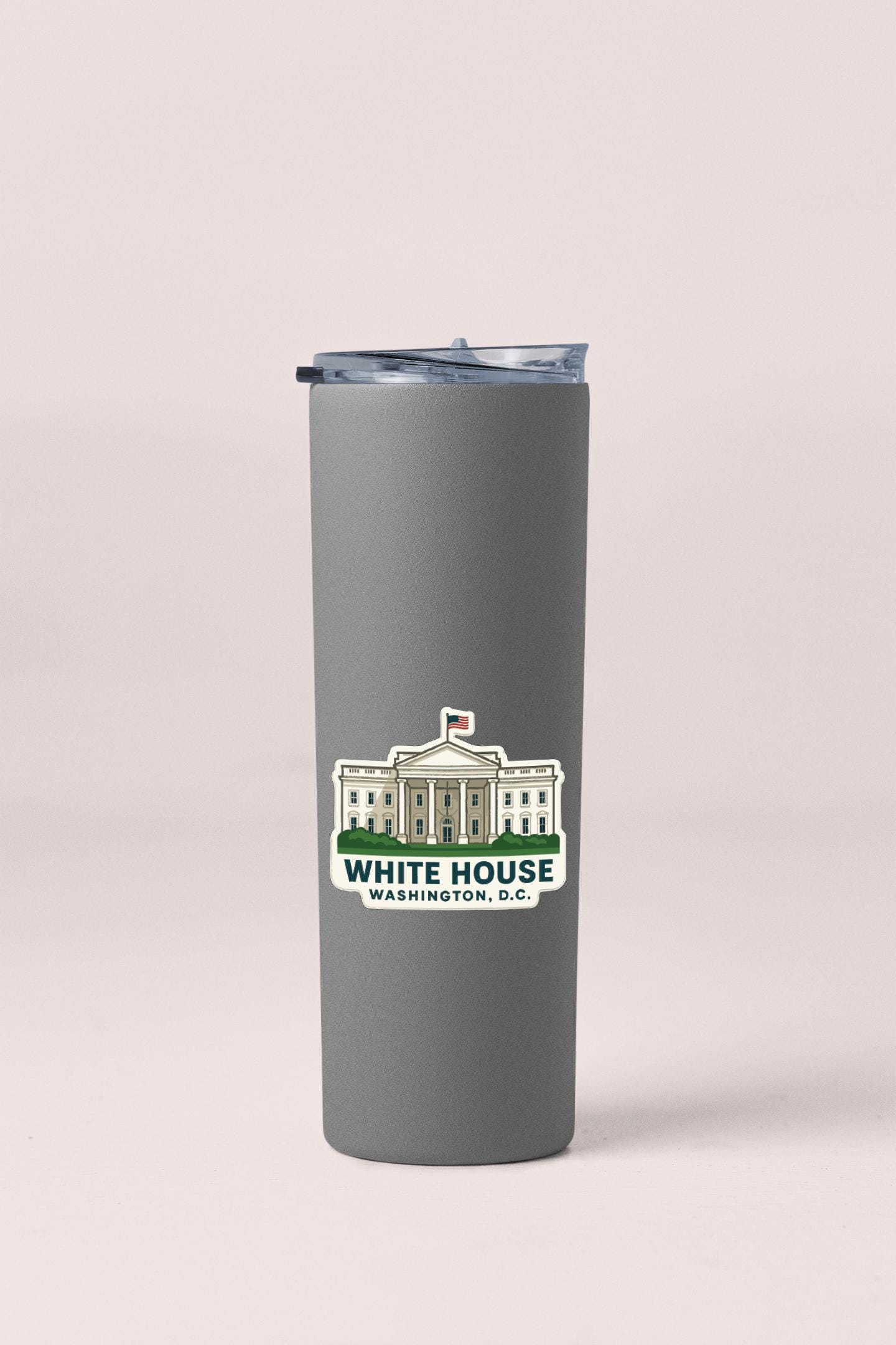 A gray insulated tumbler with a sticker depicting the White House in Washington, D.C.