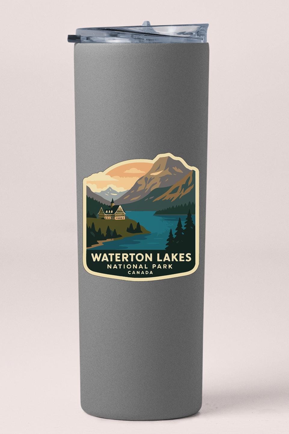 A gray tumbler with a label that features a scenic mountain landscape with a lake and a cabin, representing Waterton Lakes National Park in Canada.