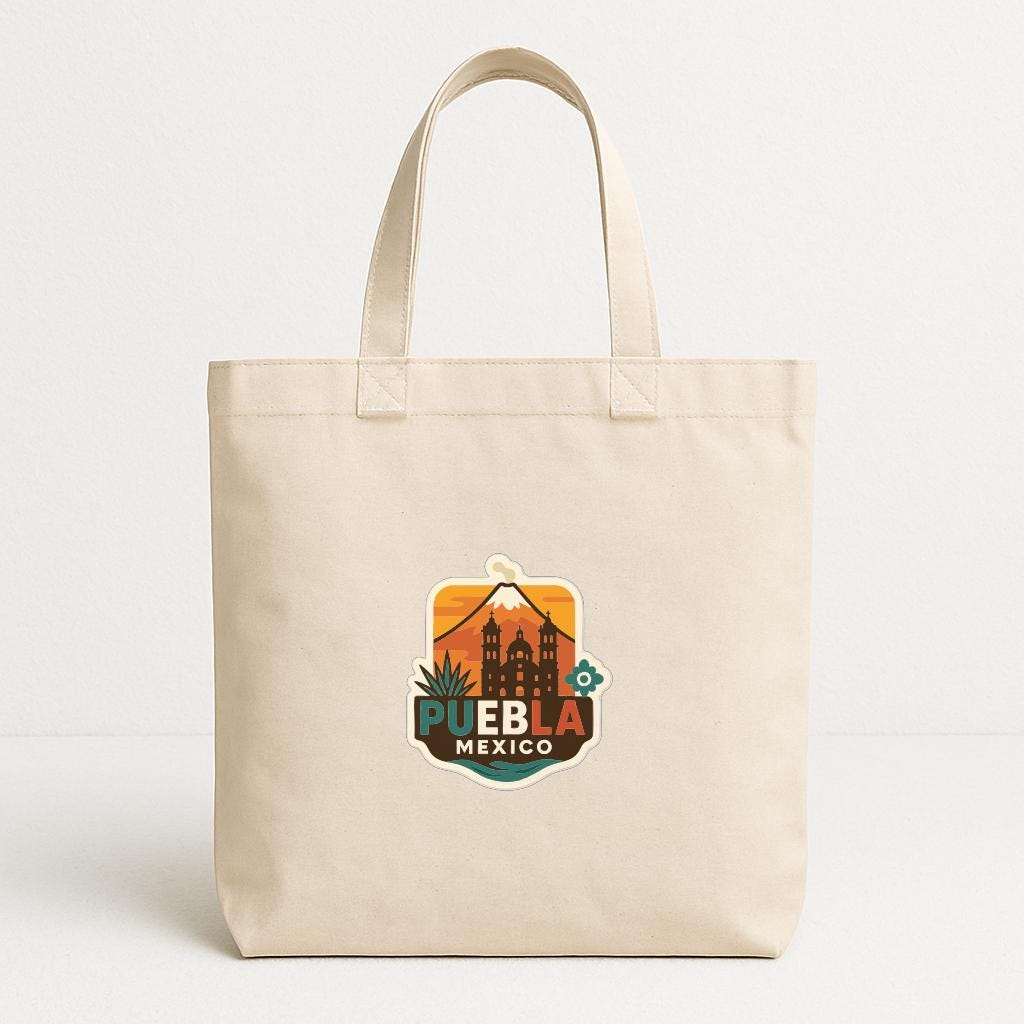 A beige tote bag with a colorful graphic of a city skyline and the text "PUEBRA MEXICO" printed on it.