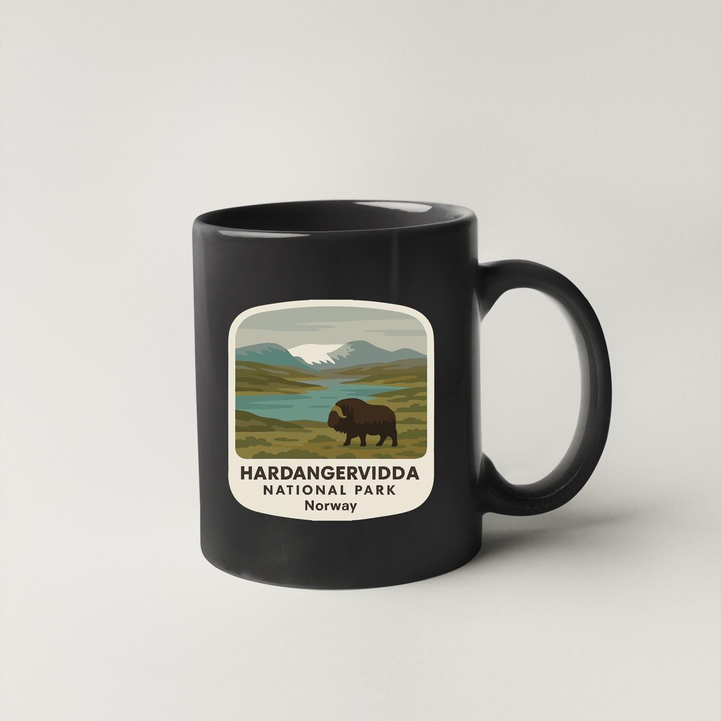 A black coffee mug with a graphic design depicting a bison in a natural landscape, along with the text "Hardangervidda NATIONAL PARK Norway".