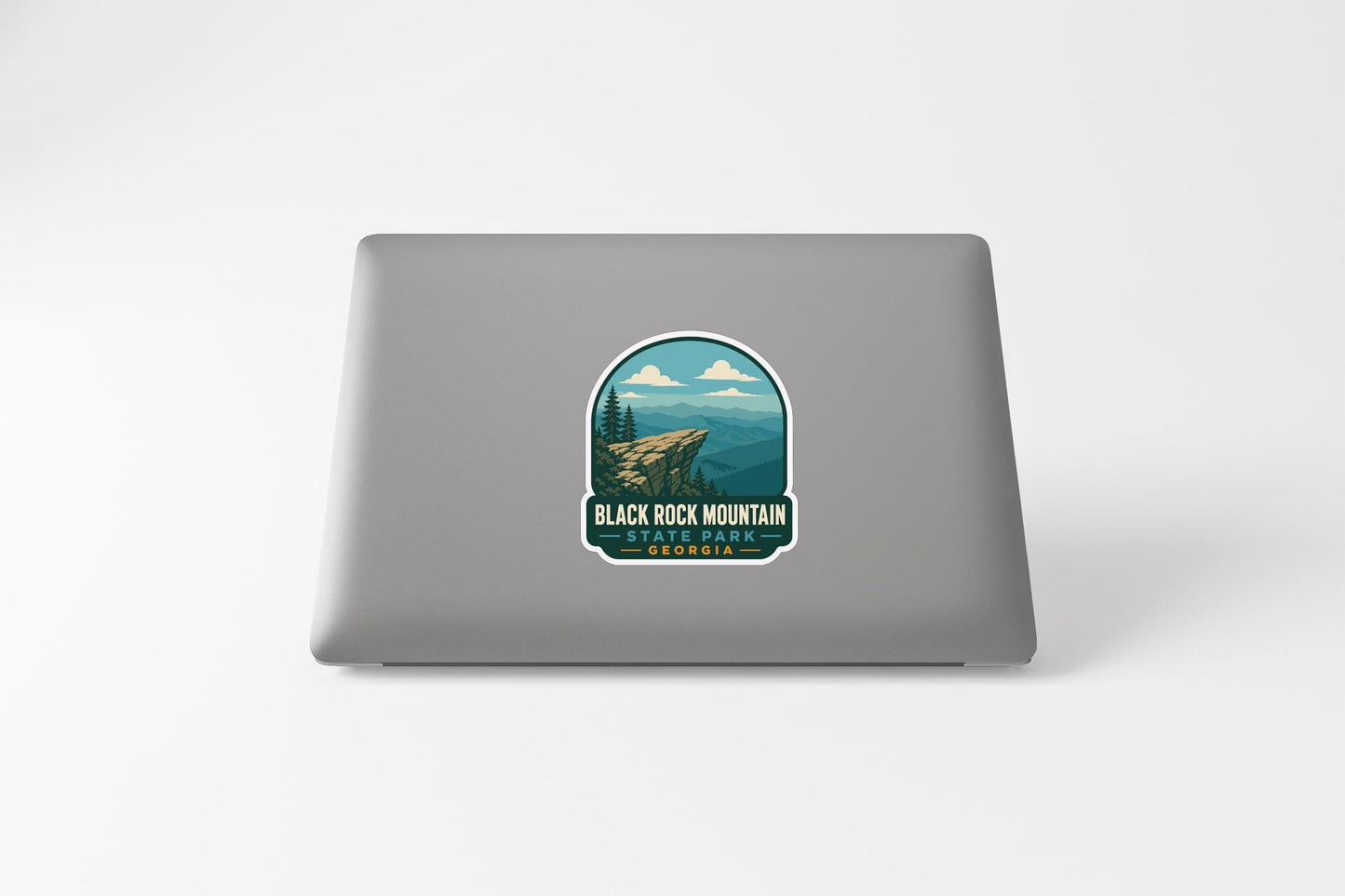 A sticker on the back of a laptop, depicting a scenic mountain landscape with a cliff and trees.