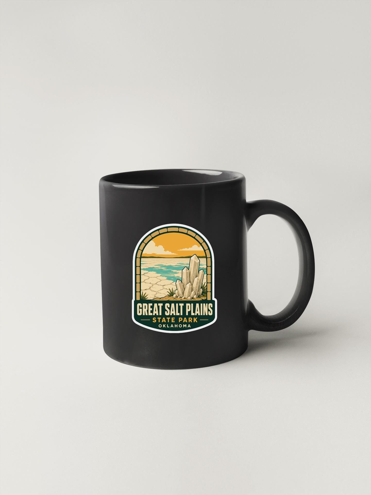 A black coffee mug with a graphic design depicting a desert landscape and the text "Great Salt Plains State Park, Oklahoma" printed on it.