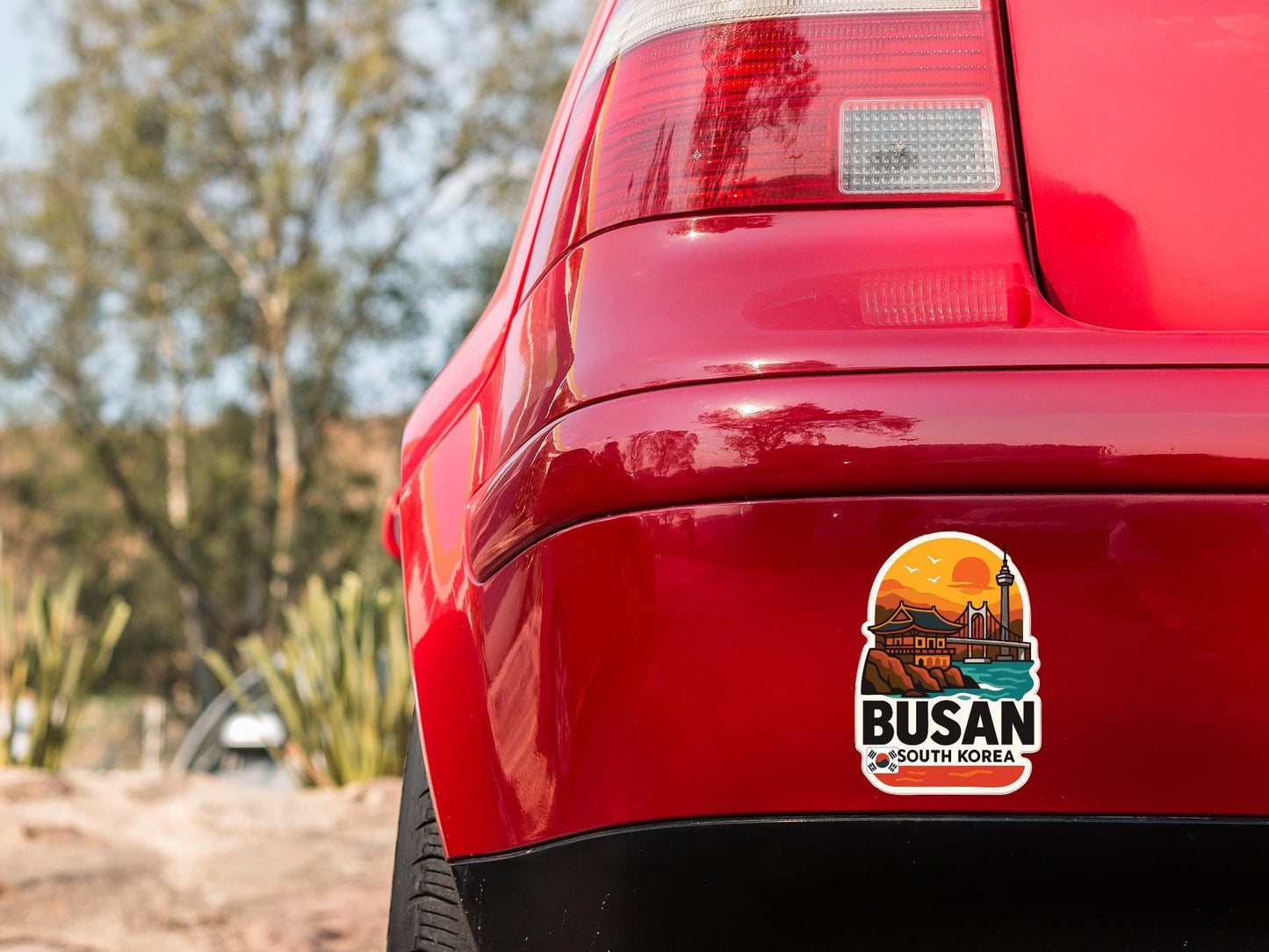the rear end of a red car with a sticker on it, featuring a scenic image of Busan, South Korea.