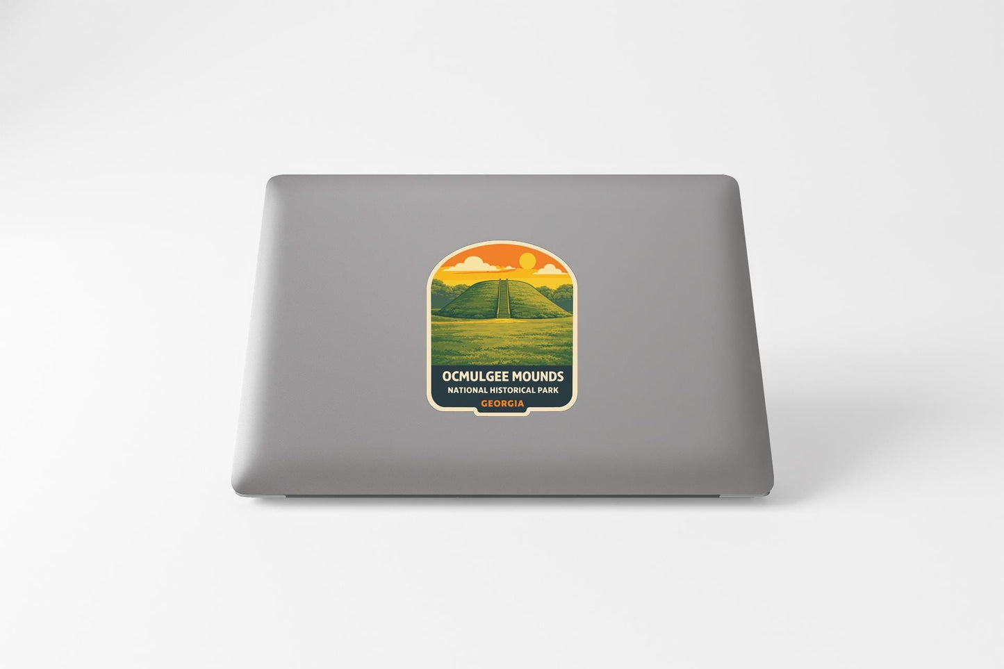 a sticker on the back of a laptop, depicting a scenic landscape with a road leading to a mountain range.