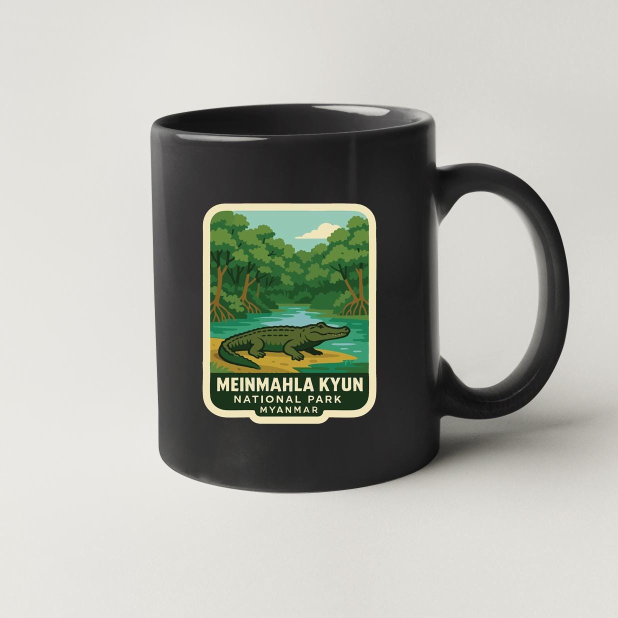 A black coffee mug with a label that features an illustration of a crocodile and the text "MEINMAHLA KYUN NATIONAL PARK VAYANG".