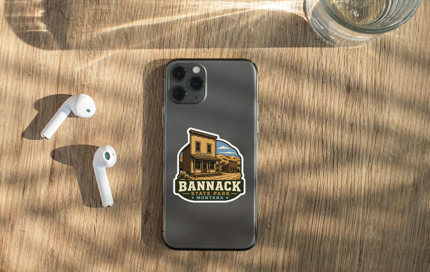 a smartphone with a sticker of a building, a pair of white earbuds, and a glass of water on a wooden surface.