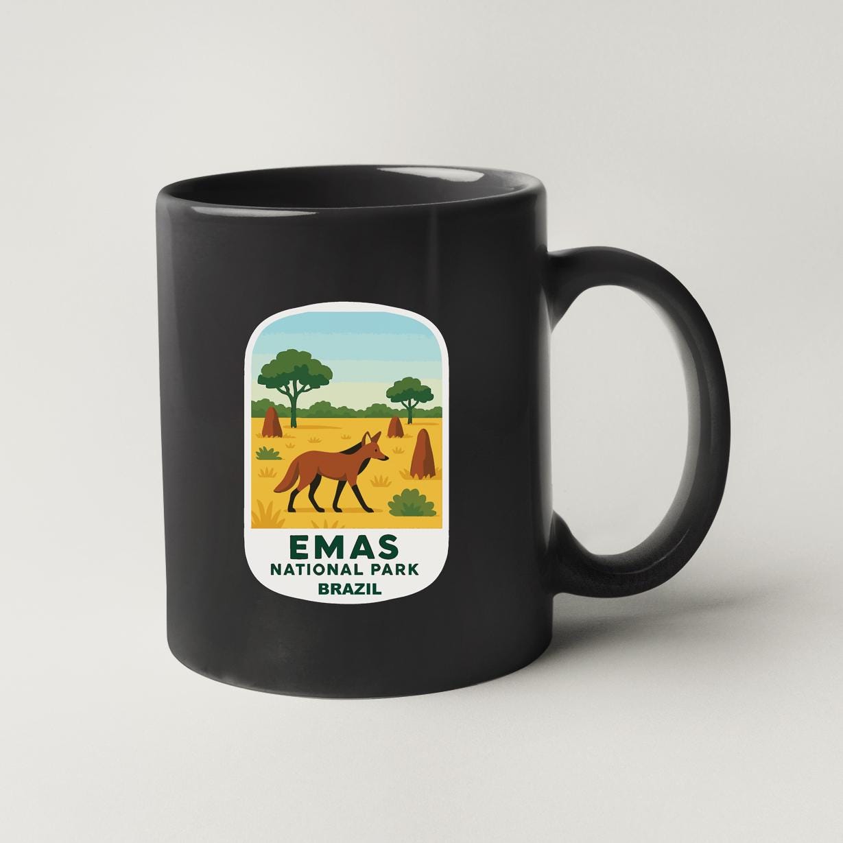 A black coffee mug with a label that features an illustration of a brown animal, likely a fox, in a grassy field with trees in the background, along with the text "EMAS NATIONAL PARK BRAZIL".