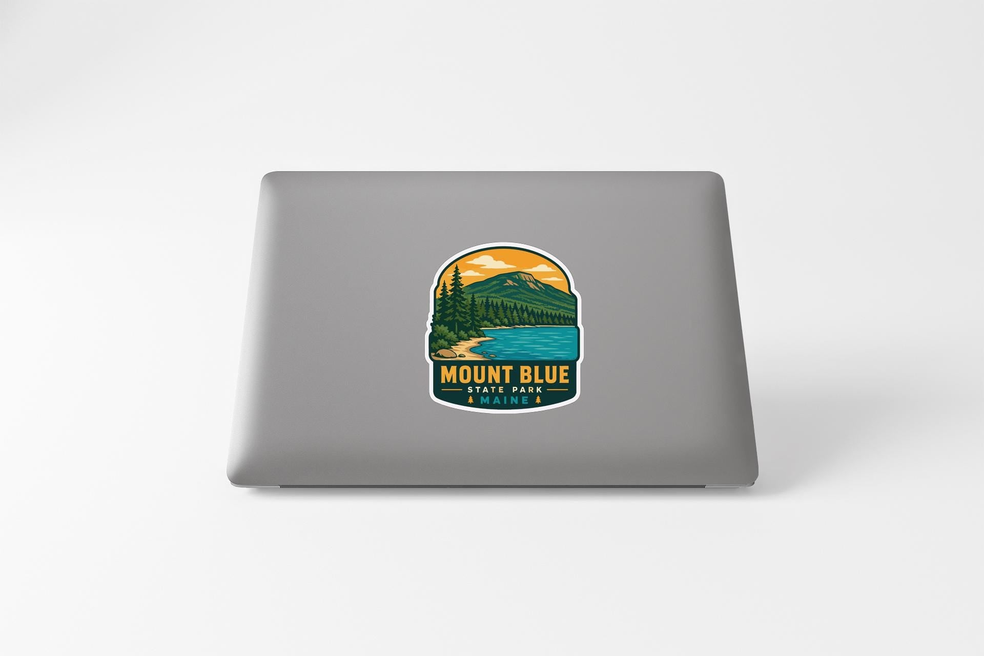 A sticker on the back of a laptop, depicting a scenic mountain landscape with a lake and pine trees.