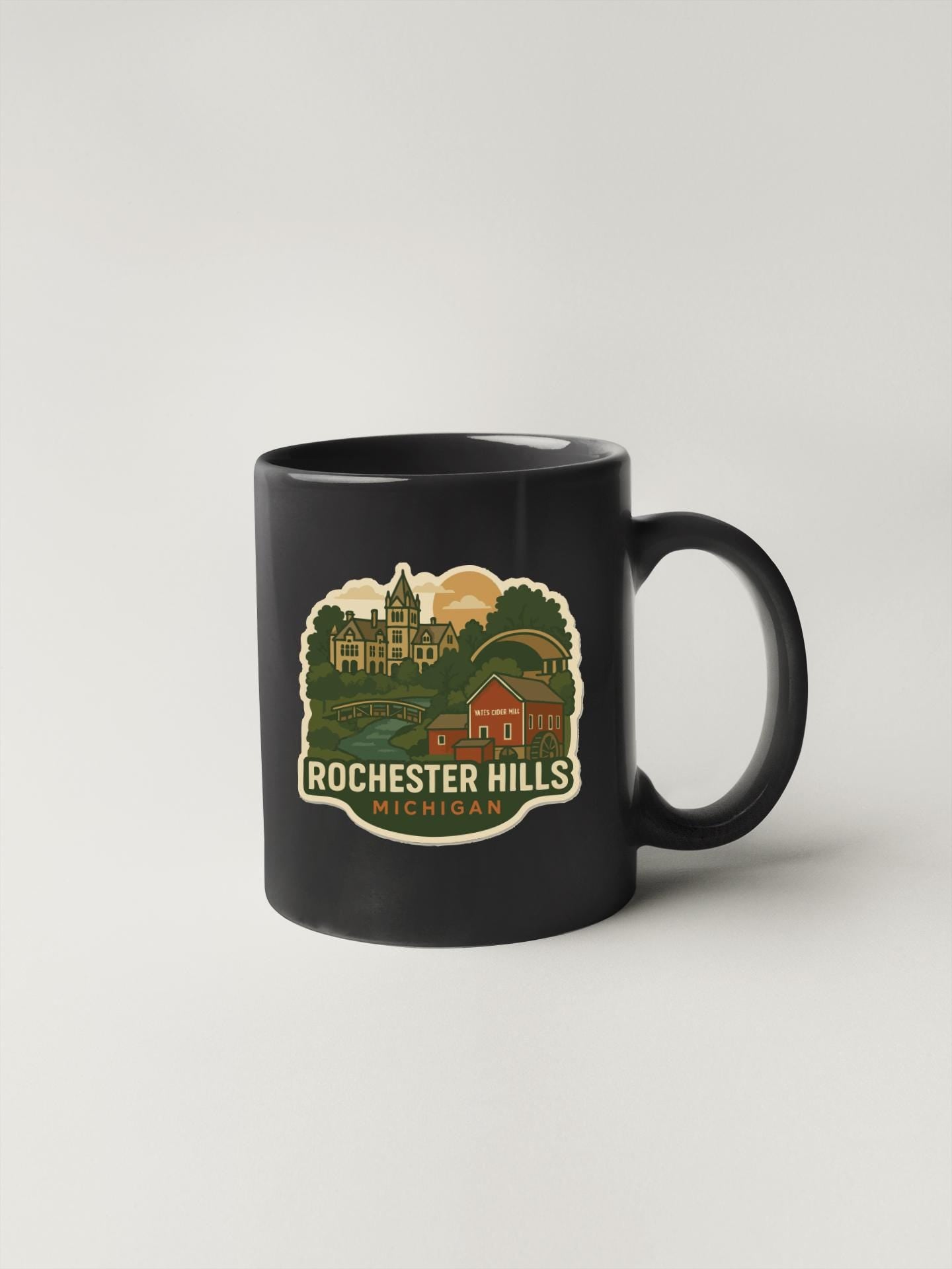 A black coffee mug with a graphic design depicting a scenic view of Rochester Hills, Michigan.