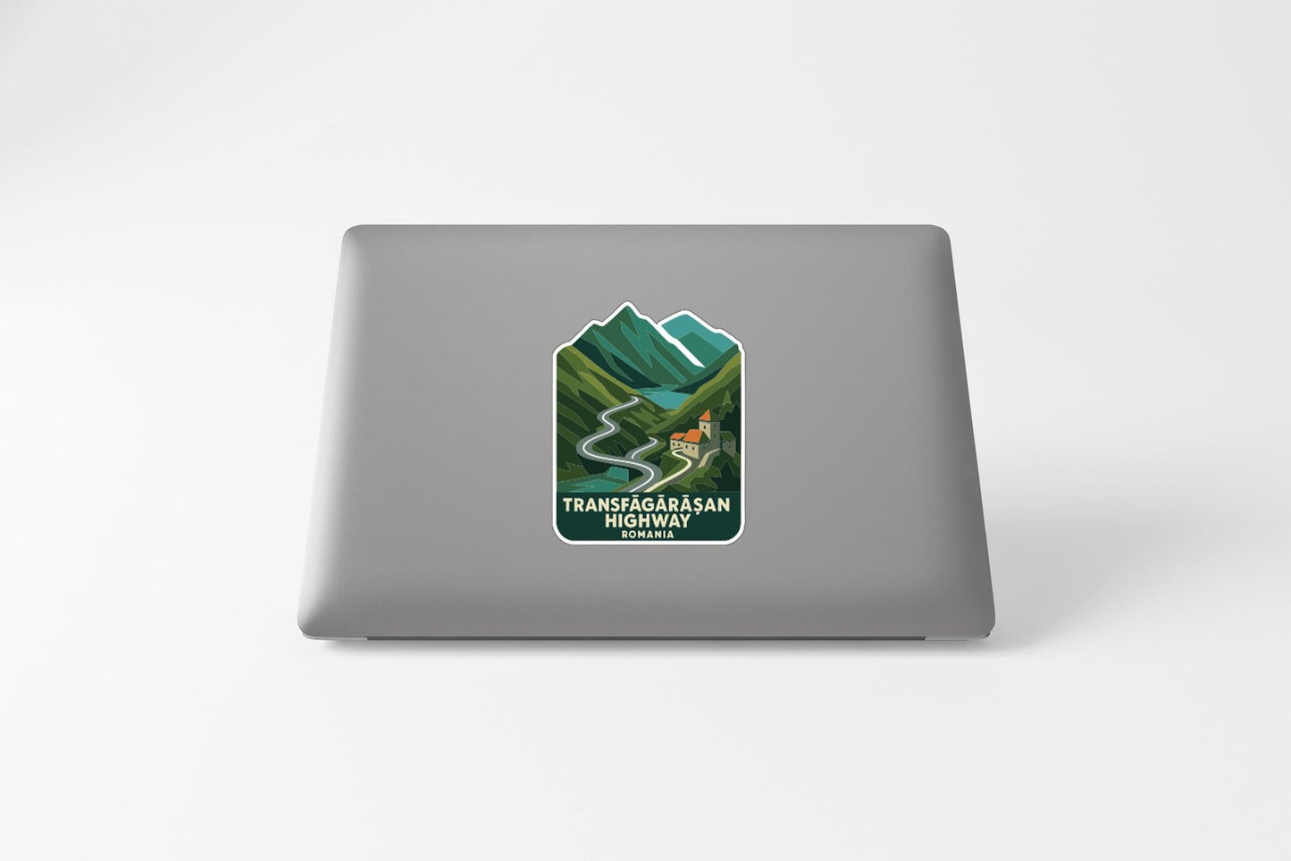 a sticker on the back of a laptop that depicts a mountain landscape with a winding road leading through it.