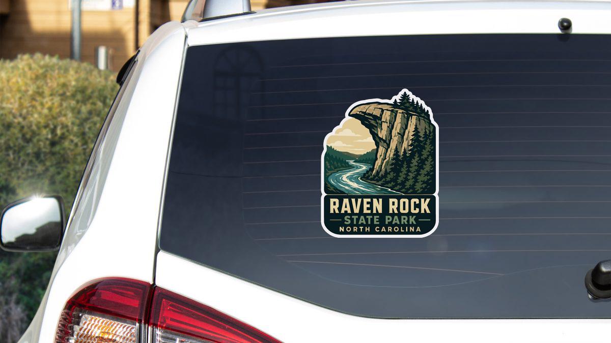 A sticker on the rear window of a white car, depicting a scenic landscape with a mountain and a river.