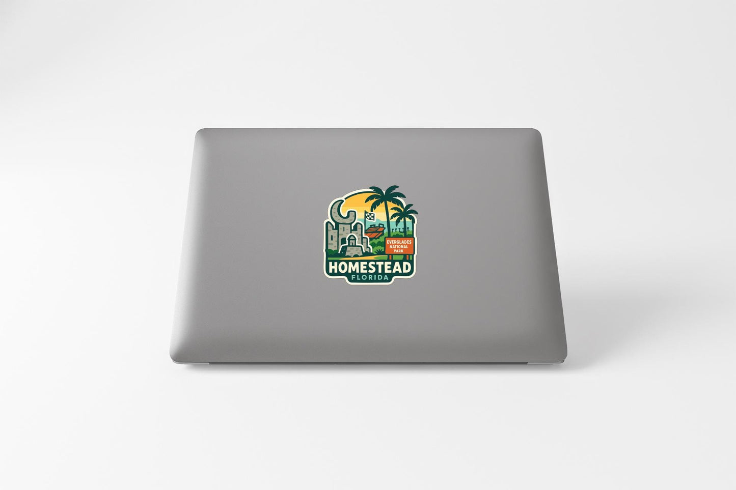 a sticker or decal on the back of a laptop, depicting a tropical scene with palm trees, a building, and a sunset.