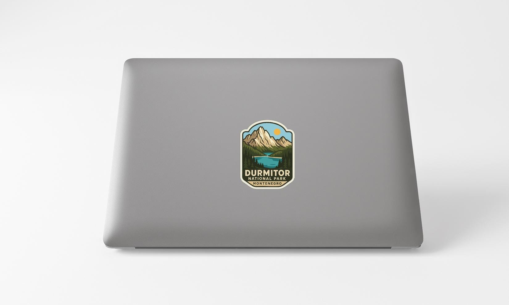 A sticker with a mountain landscape and a lake on the back of a laptop computer.