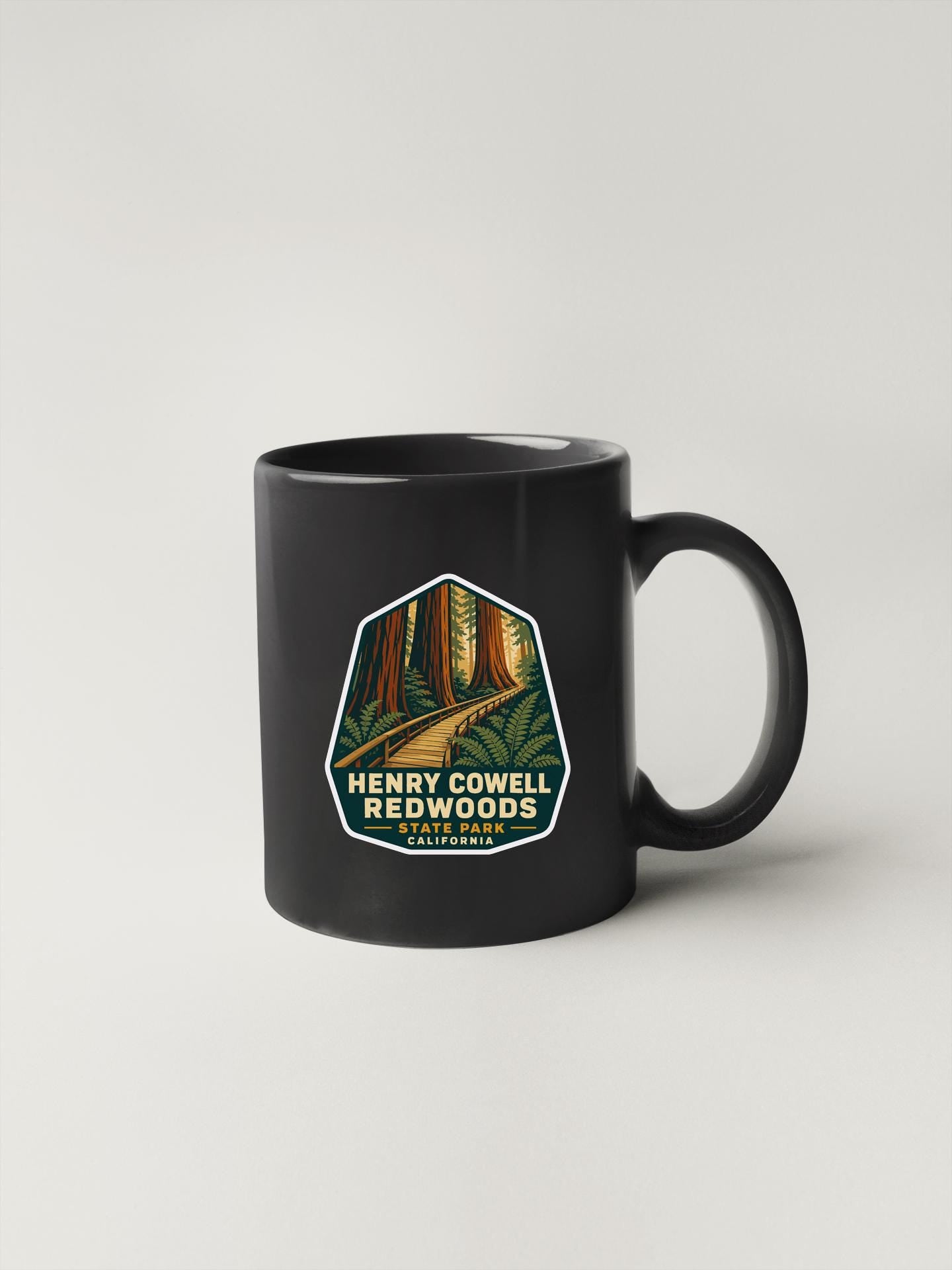 A black coffee mug with a graphic design featuring a forest scene and the text "Henry Cowell Redwoods State Park California".