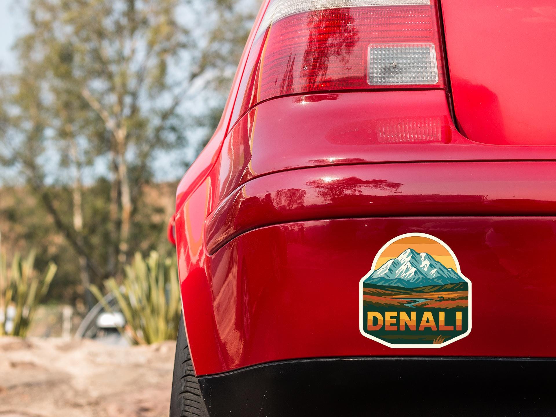 the rear end of a red car with a sticker on the trunk that says "DENALI".