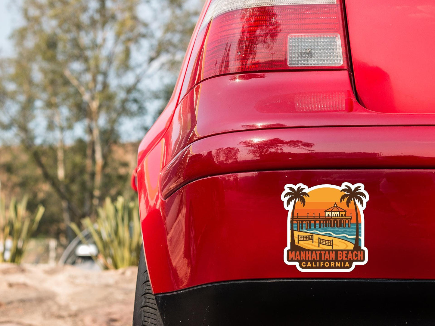 the rear end of a red car with a sticker on the trunk that says "MANHATTAN BEACH CALIFORNIA".
