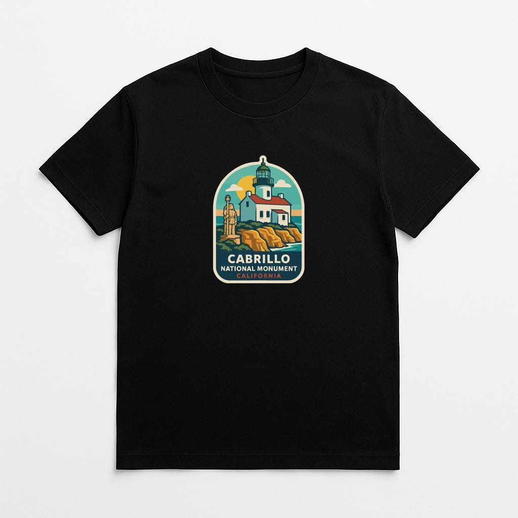 A black t-shirt with a graphic design depicting a lighthouse and a building, along with the text "CABRILLO NATIONAL MONUMENT".