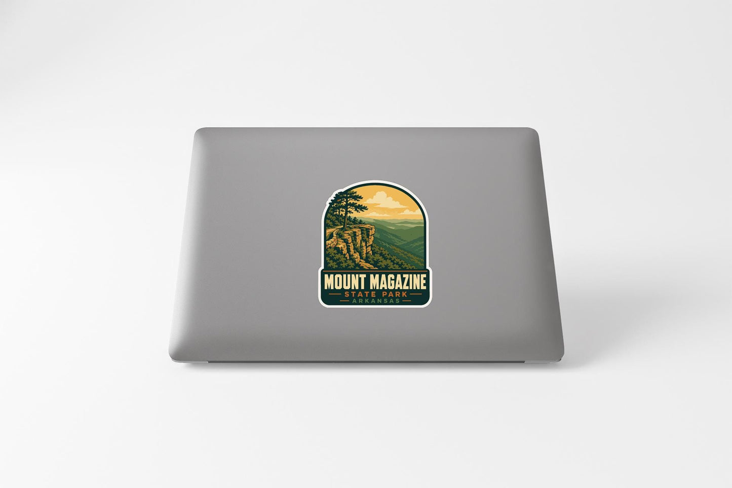 A sticker on the back of a laptop that features a scenic landscape with mountains and a sunset.