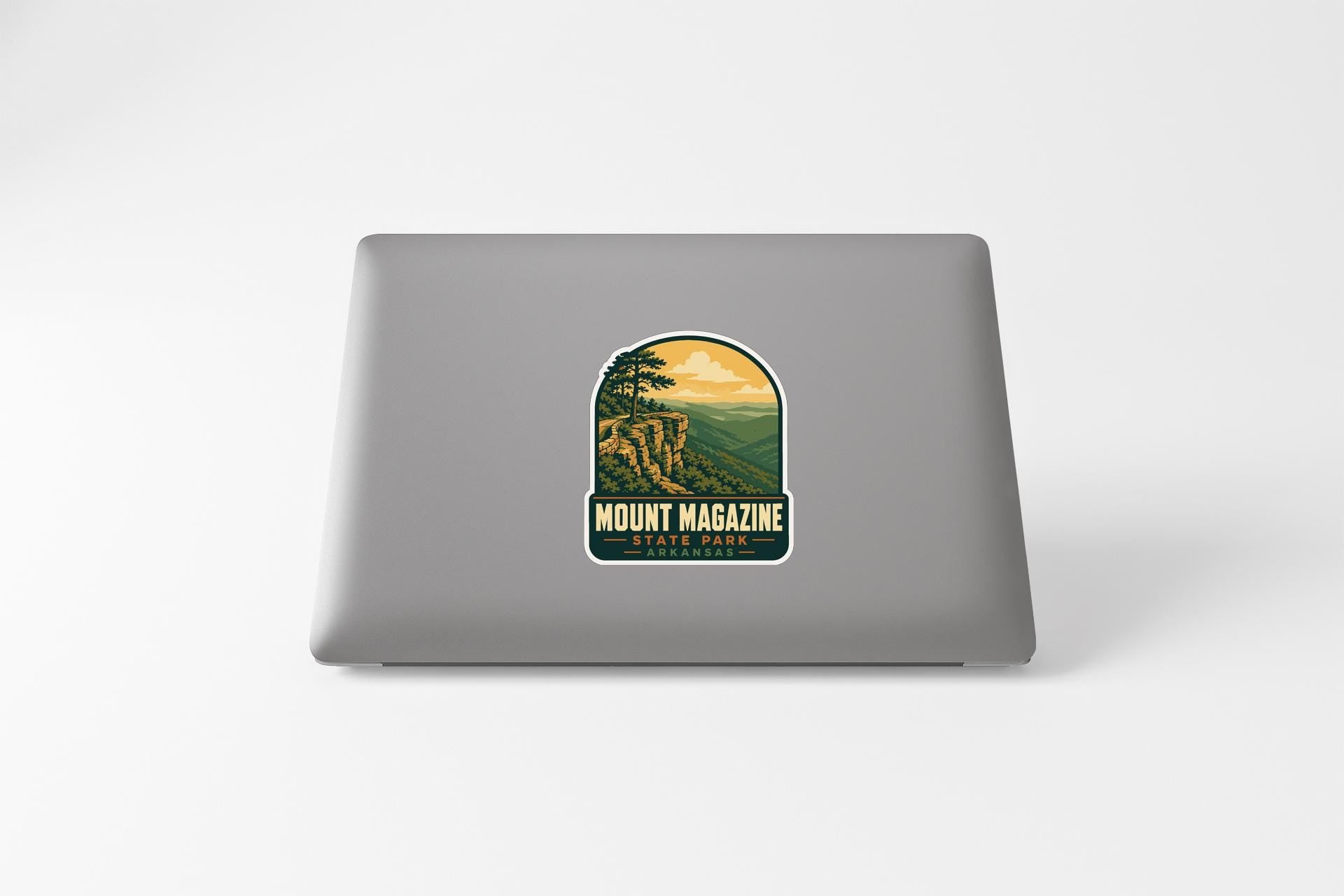 A sticker on the back of a laptop that features a scenic landscape with mountains and a sunset.