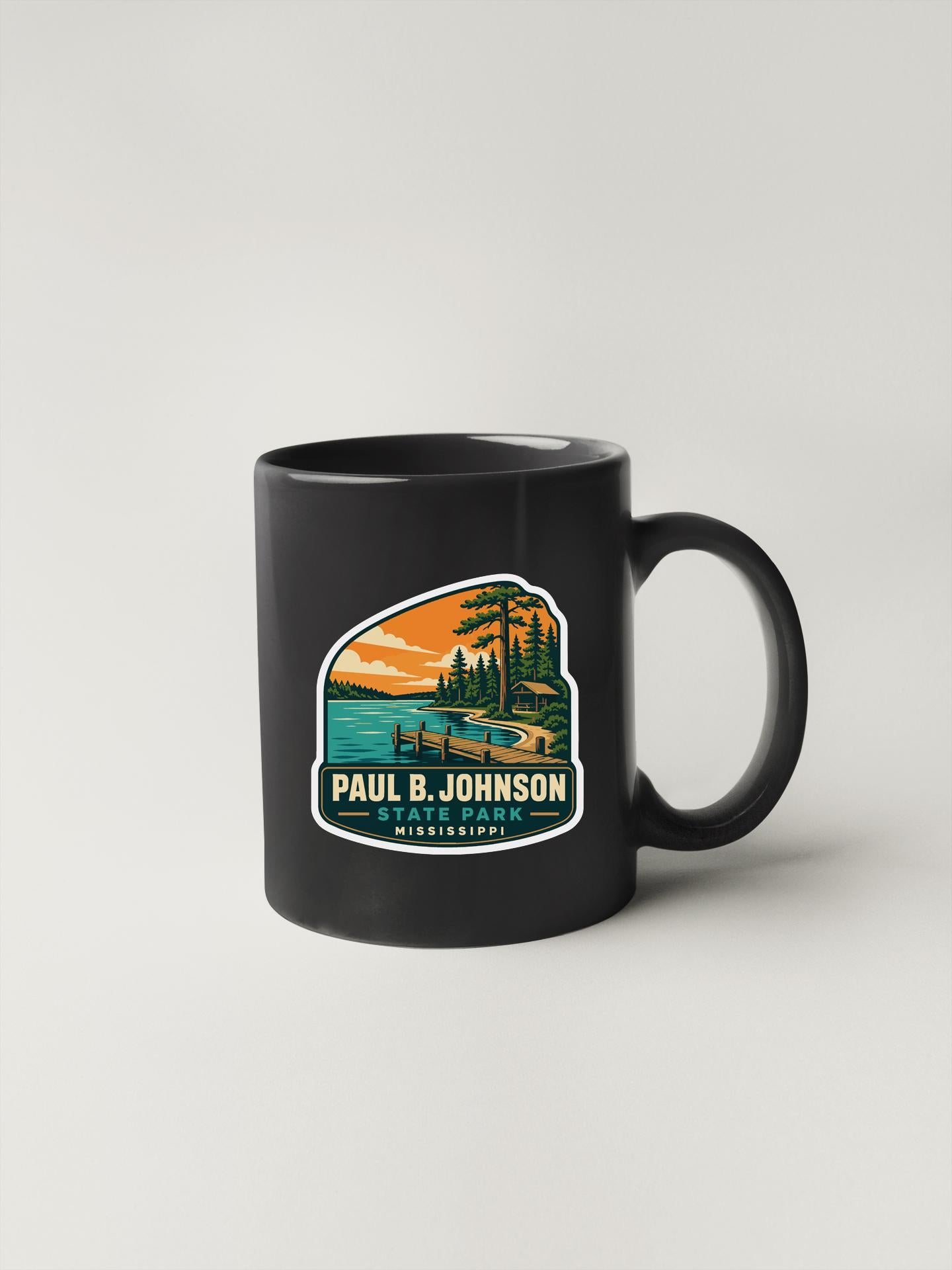 A black coffee mug with a colorful graphic depicting a scenic landscape, including a lake, mountains, and trees.