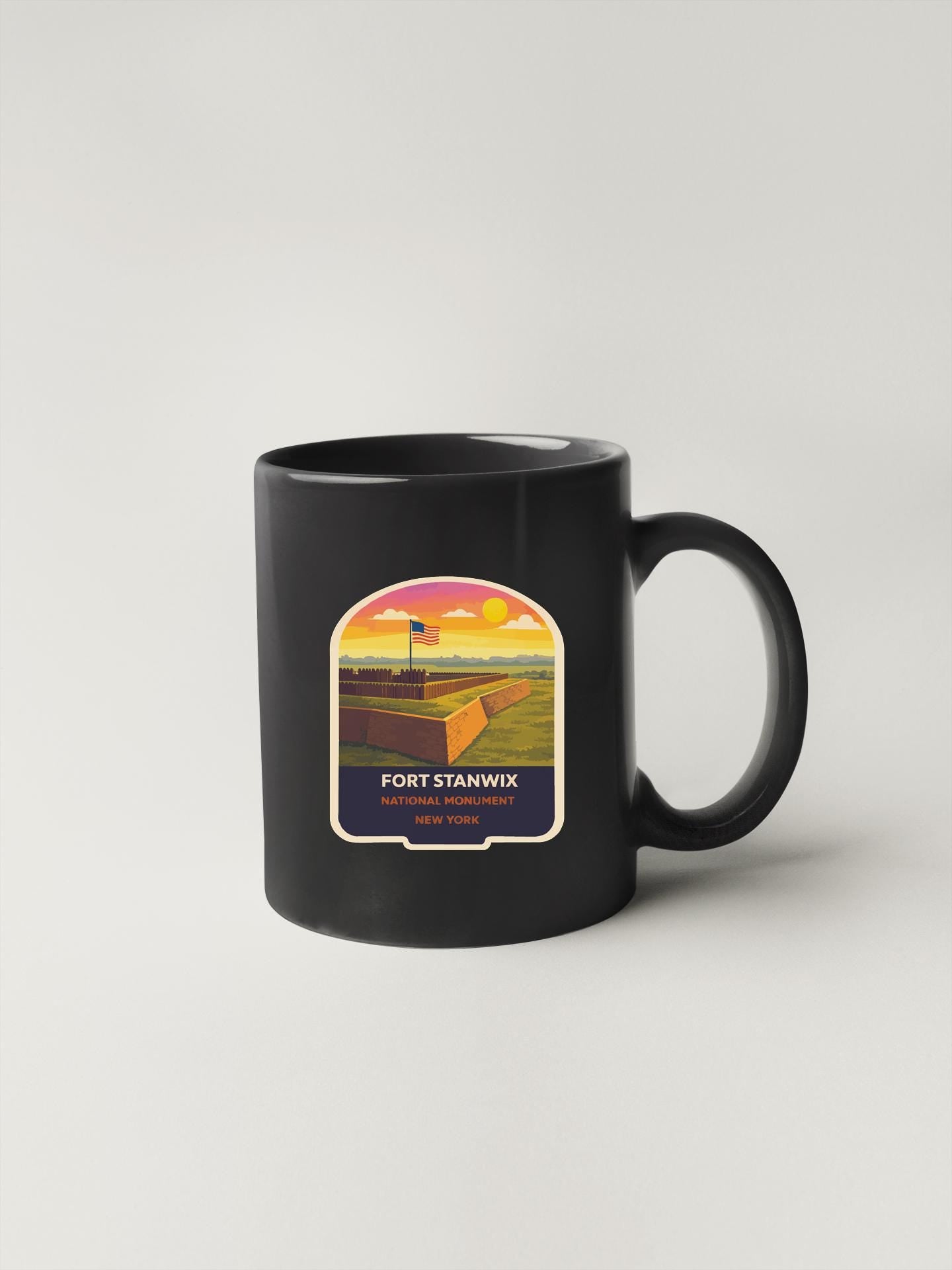 A black coffee mug with a label that says "FORT STANWIX NEW YORK" and features an illustration of a fort or military structure.