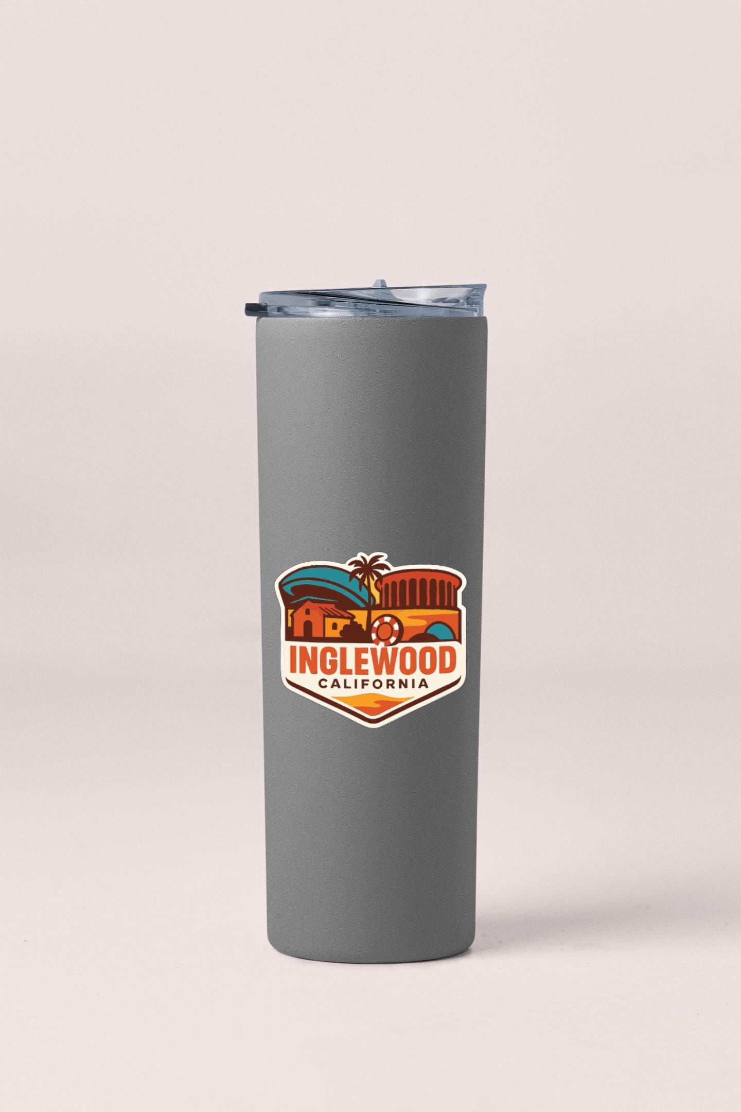 A gray insulated tumbler with a lid and a sticker featuring the text "INGLEWOOD CALIFORNIA" and an illustration of a building.